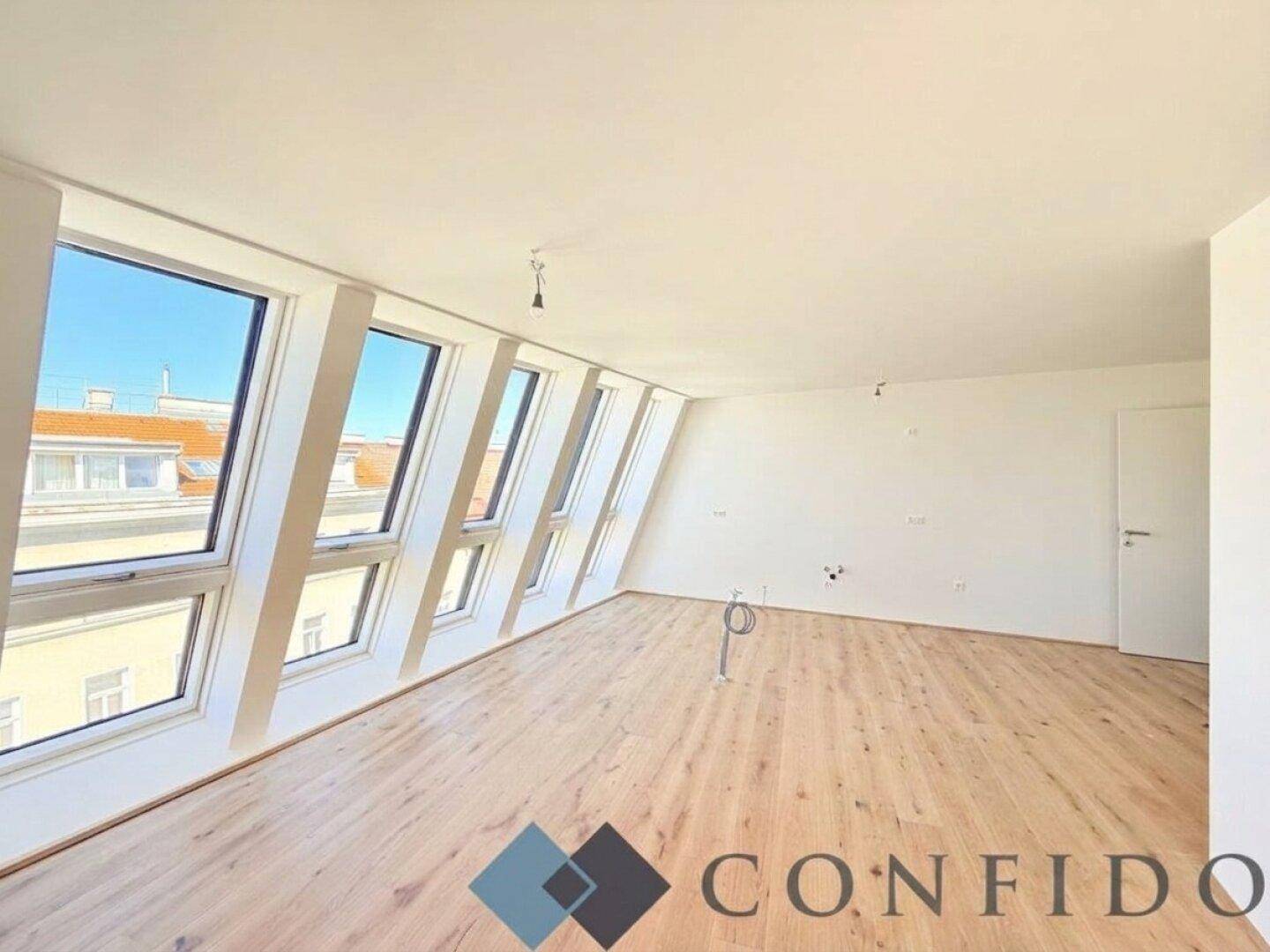 Heller Wohnraum mit Holzboden und schrägen Wänden, beleuchtet durch mehrere Dachfenster.