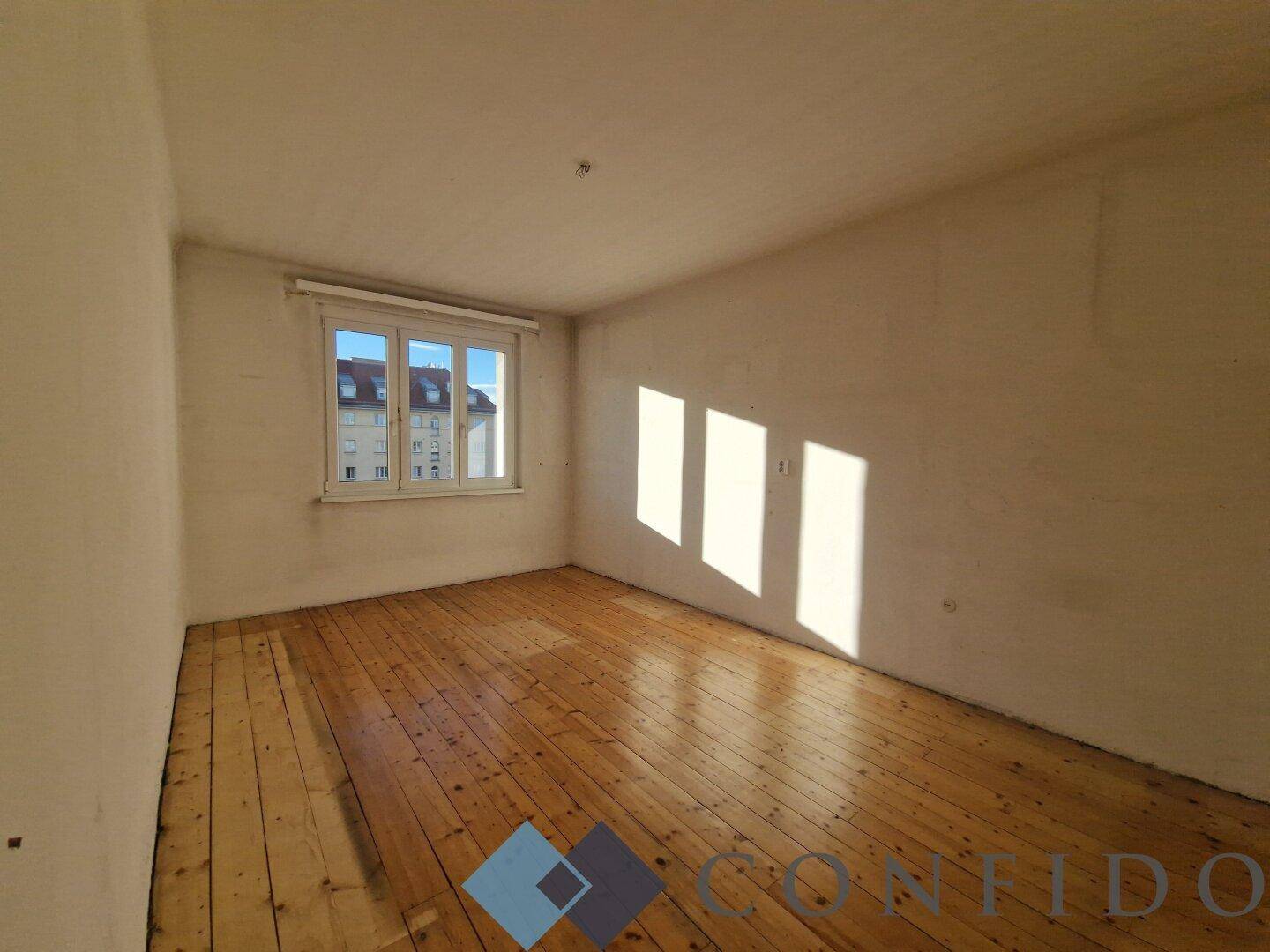 Sonniger Raum mit Holzdielenboden und hellen Wänden, ideal als Schlafzimmer.