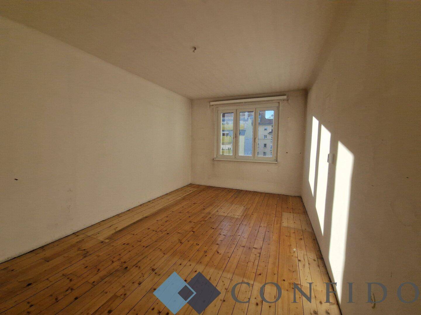 Heller Raum mit Holzdielenboden und Fenster, das viel Tageslicht hereinlässt.