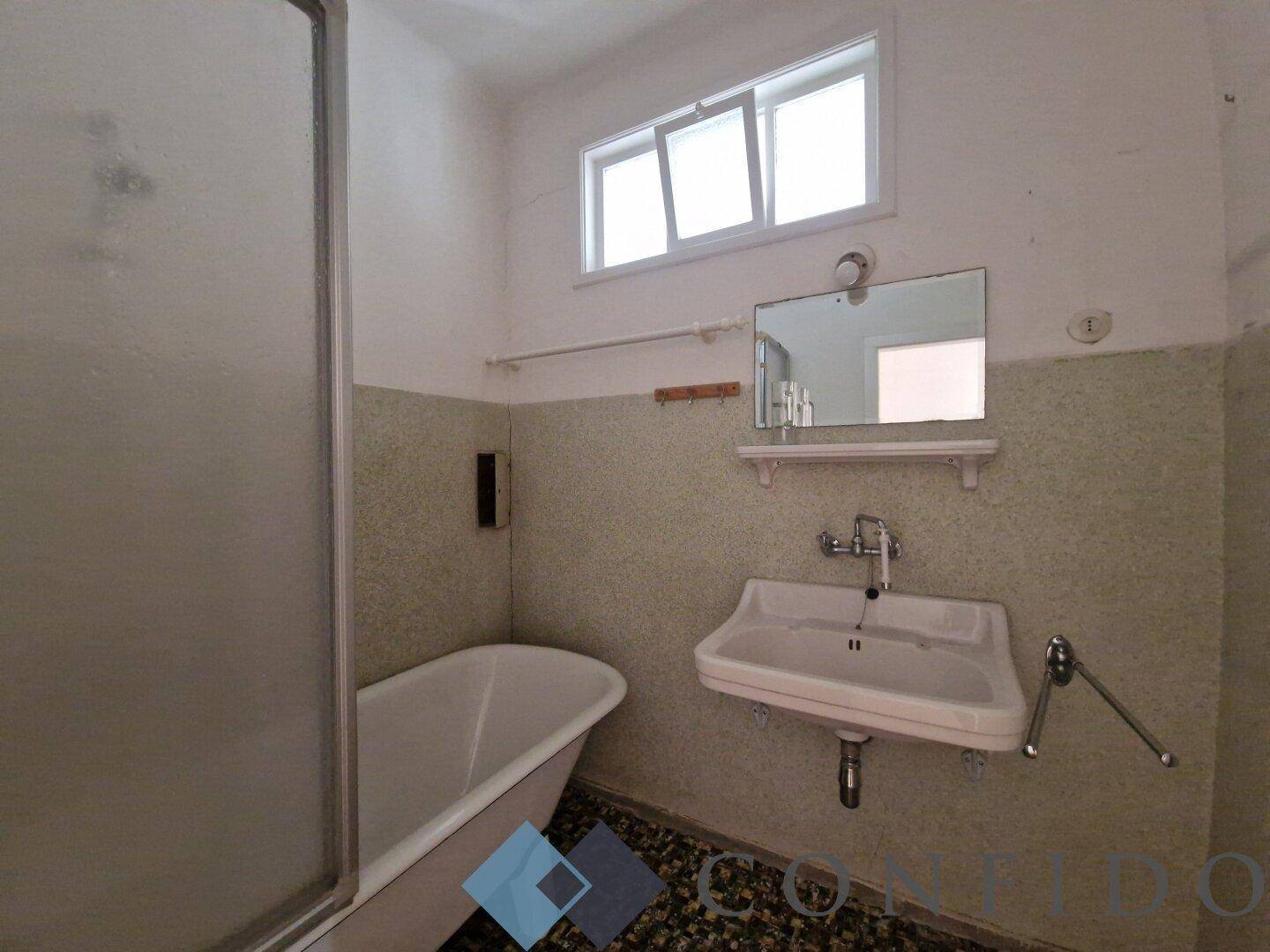 Badezimmer mit Badewanne, Waschbecken und einem kleinen Fenster für Belüftung.