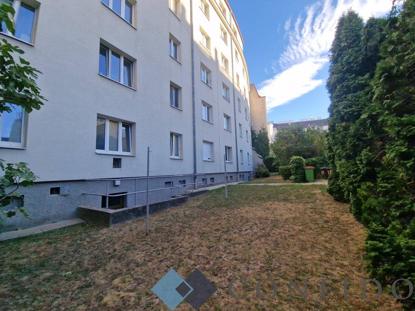 Gepflegter Gemeinschaftsgarten neben dem Wohngebäude mit Bäumen und Rasenfläche.