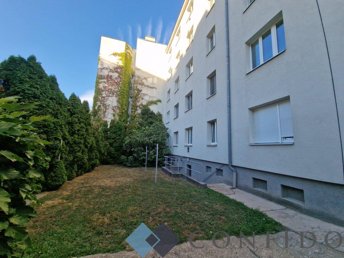 Außenansicht des Gebäudes mit einem grünen Gartenbereich und Zugang zum Keller.