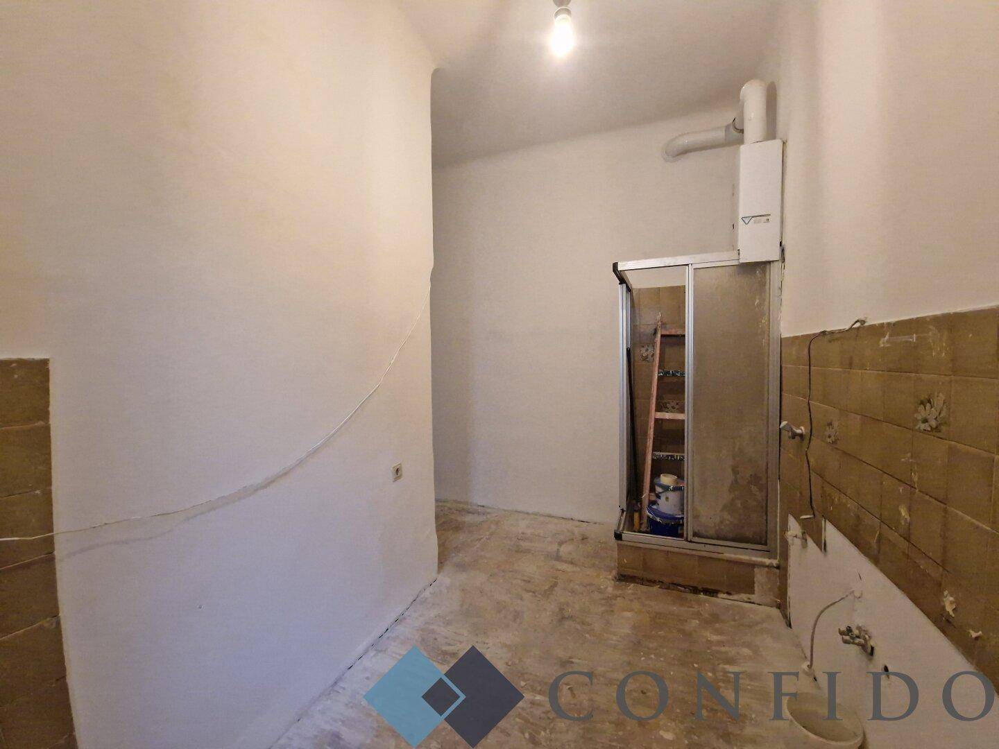 Badezimmer im Rohbauzustand mit Duschkabine und sichtbaren Installationen, bereit zur Renovierung.