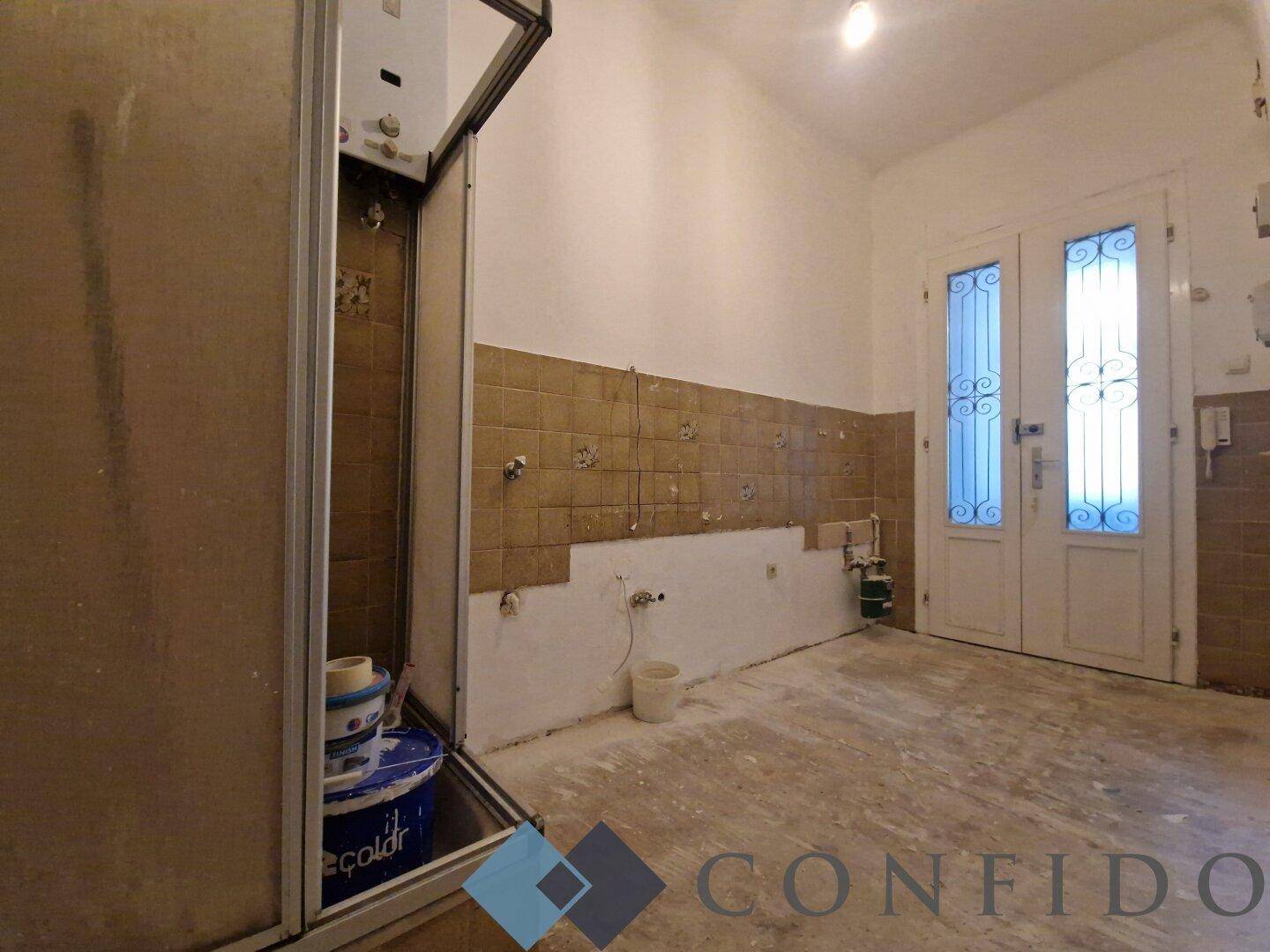 Badezimmer im Rohbau mit alten Fliesen und Duschkabine, Blick zur Eingangstür.