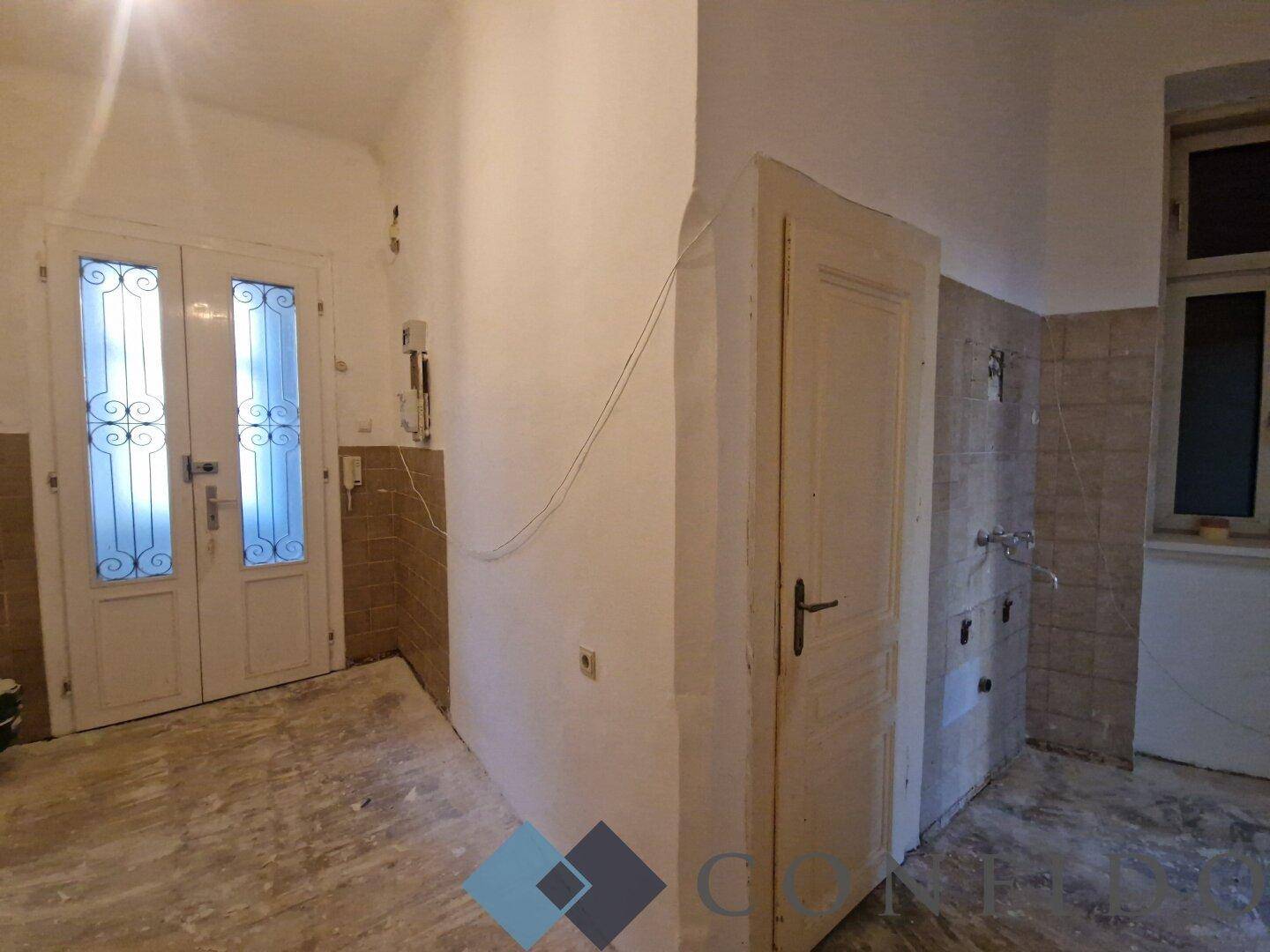 Badezimmer im Rohbauzustand mit alter Tür und Fliesen, bereit für eine Modernisierung.