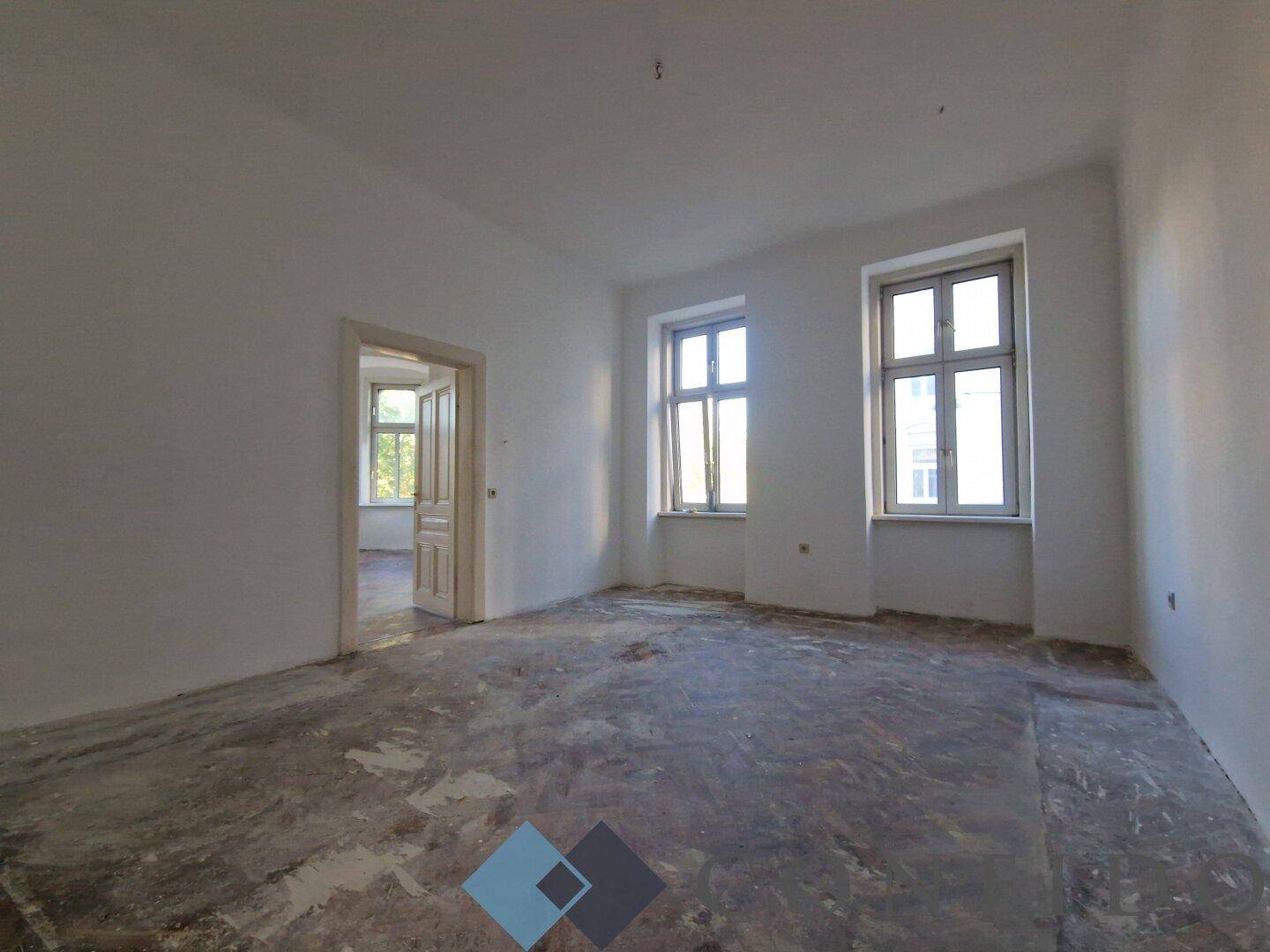 Heller Wohnraum im Rohbau mit zwei großen Fenstern und Blick auf die Umgebung.