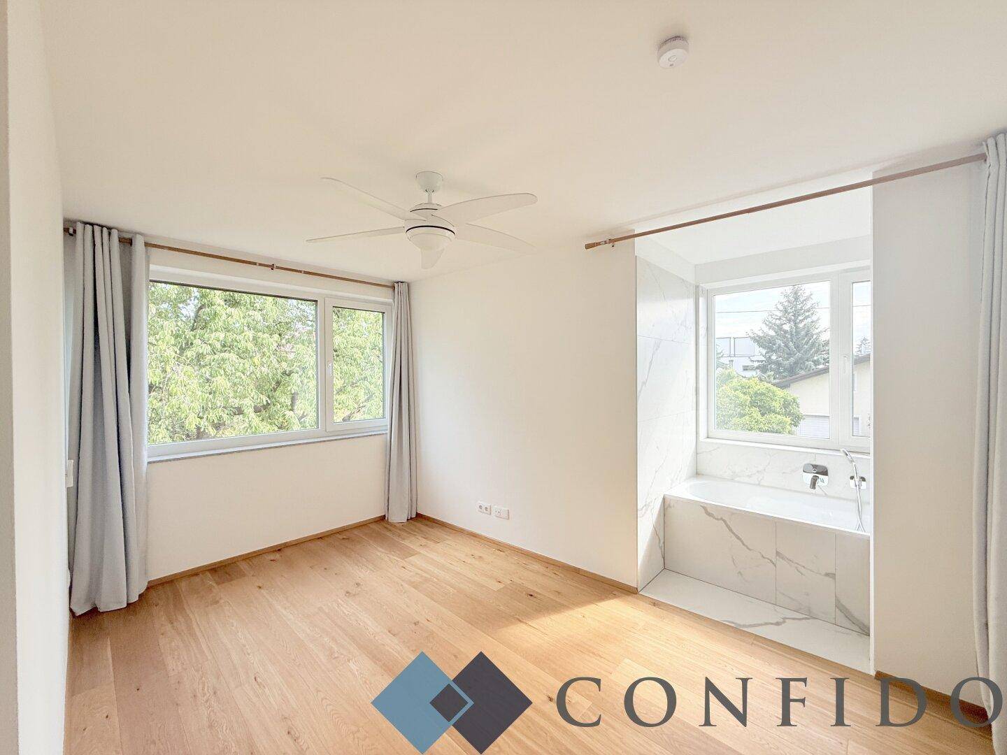 Geräumiges Schlafzimmer mit Holzboden, Deckenventilator und integrierter Badewanne am Fenster.