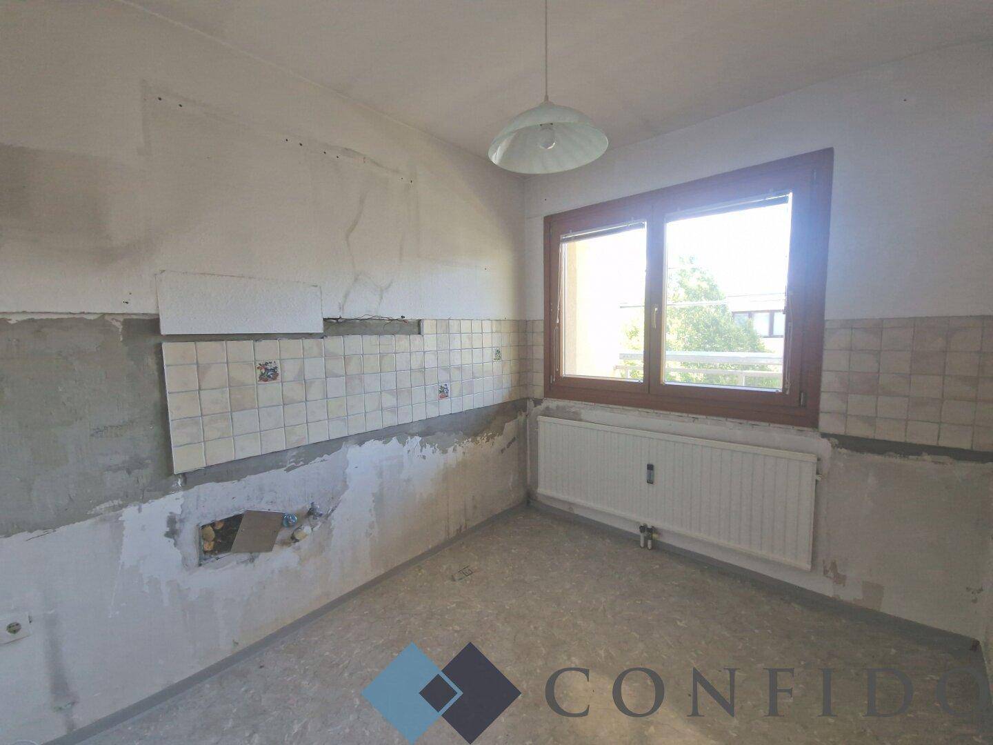 Küche in Renovierung mit alten Fliesen und Fenster, bereit für eine neue Gestaltung.
