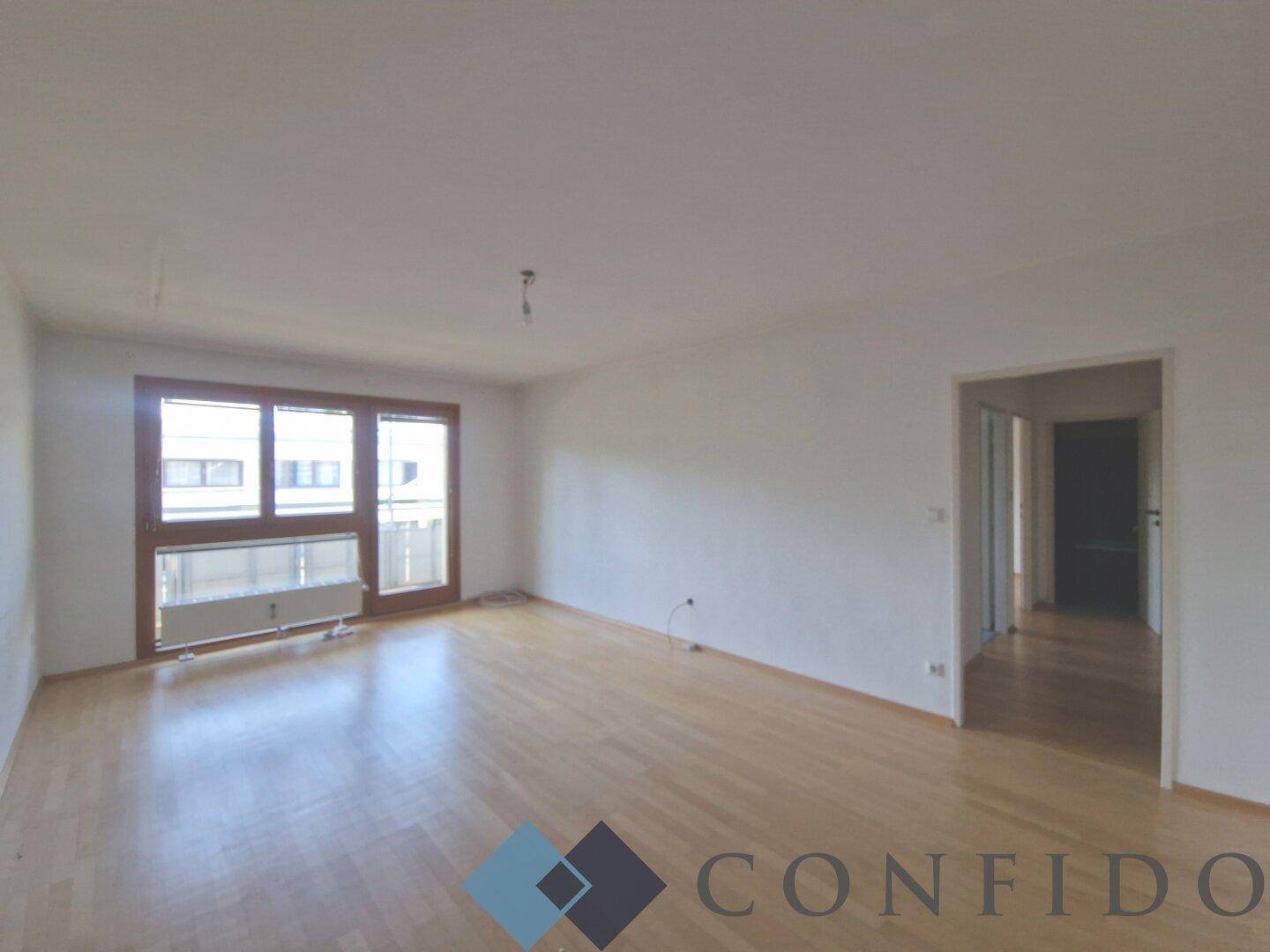Geräumiges, helles Zimmer mit Holzboden und großen Fenstern, bietet viel Tageslicht.