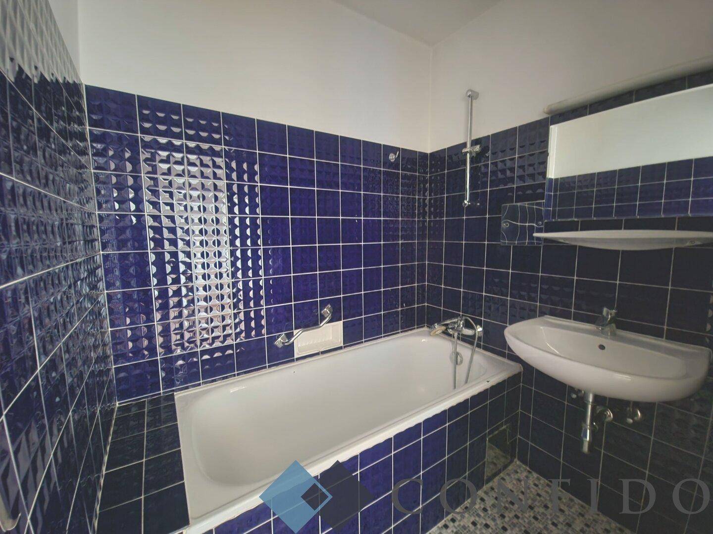 Badezimmer mit blauen Fliesen, Badewanne und Waschbecken, im Stil der 80er Jahre.