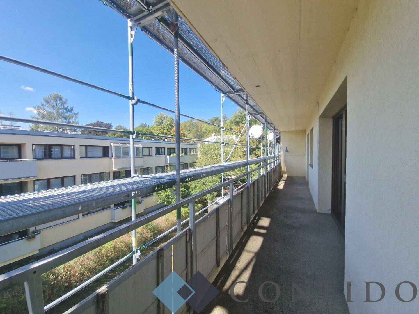 Langer Balkon mit Gerüst, bietet Blick auf die umliegenden Gebäude und Grünflächen.