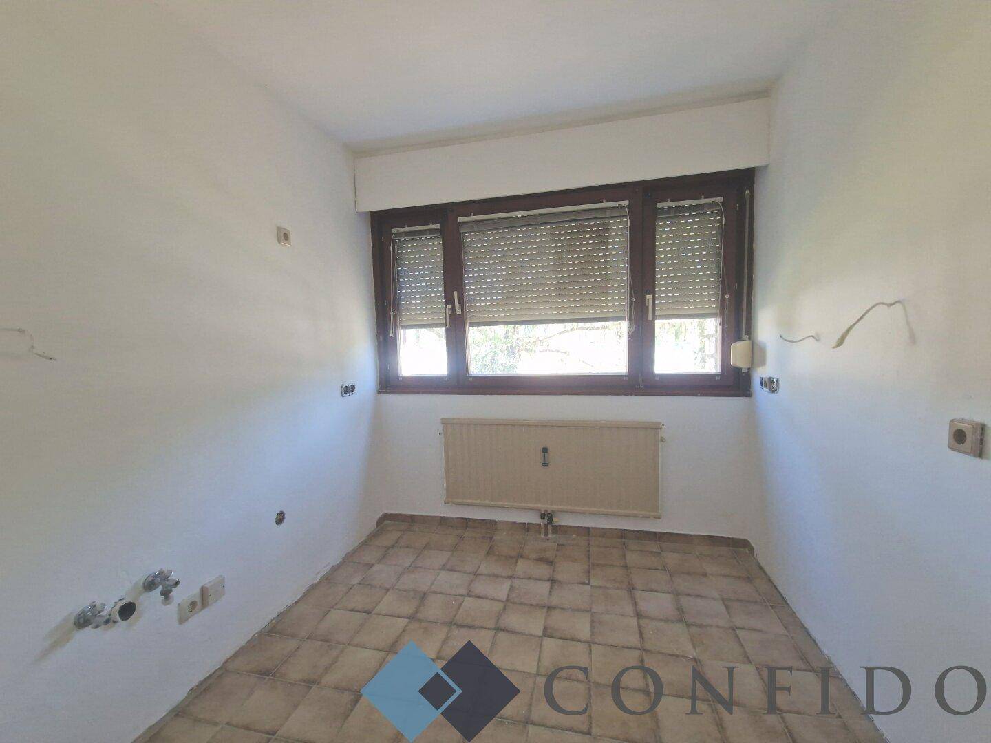 Küche mit Fliesenboden und Fenster, vorbereitet für die Installation einer neuen Einbauküche.