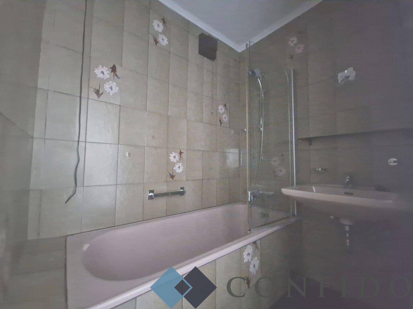 Badezimmer mit Badewanne und Waschbecken, ausgestattet mit älteren Fliesen und Armaturen.