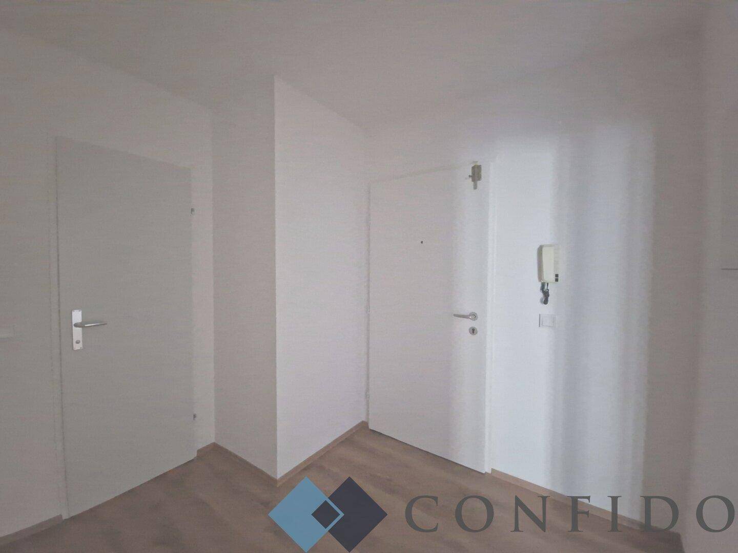 Eingangsbereich mit Laminatboden, weißen Türen und Gegensprechanlage, empfängt Bewohner und Gäste.