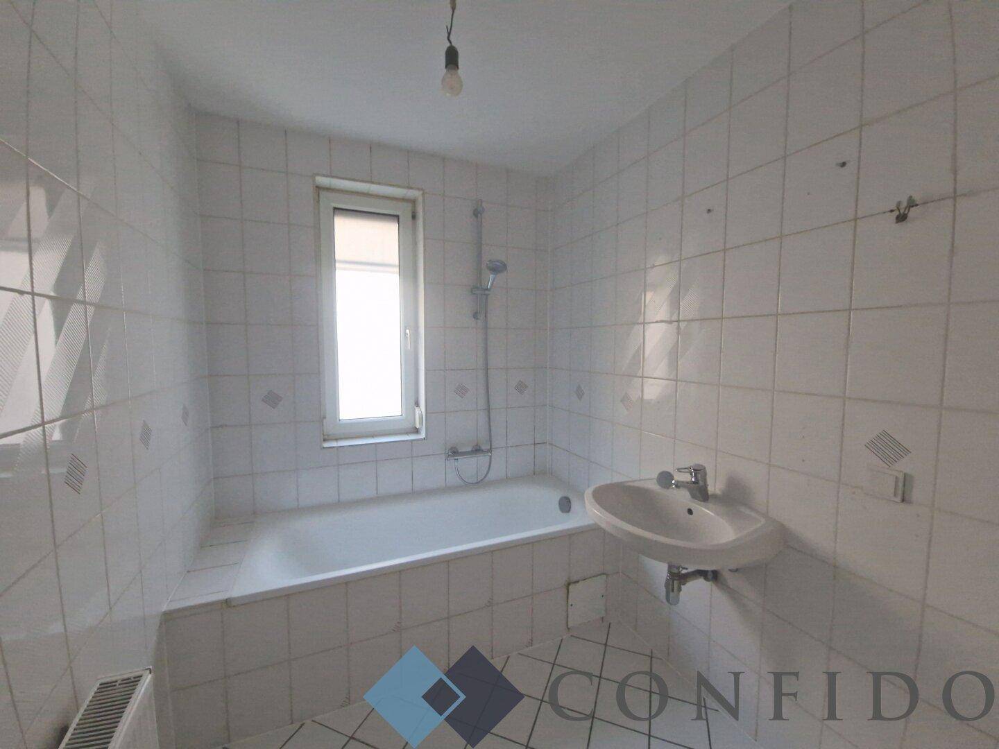 Gefliestes Badezimmer mit Badewanne, Waschbecken und Fenster, bietet ausreichend Tageslicht.