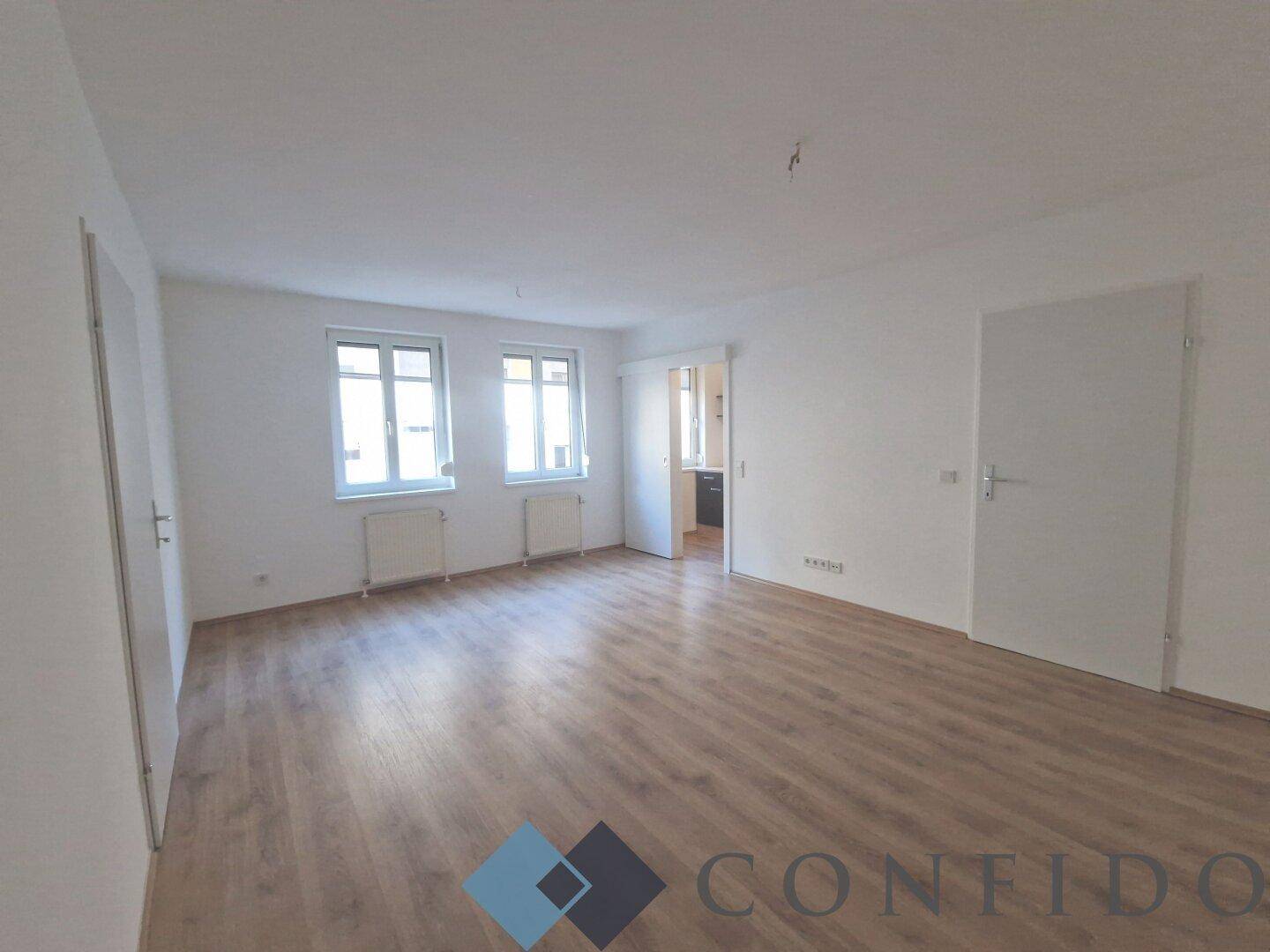 Geräumiges, helles Wohnzimmer mit Laminatboden und zwei Fenstern, bietet viel natürliches Licht.