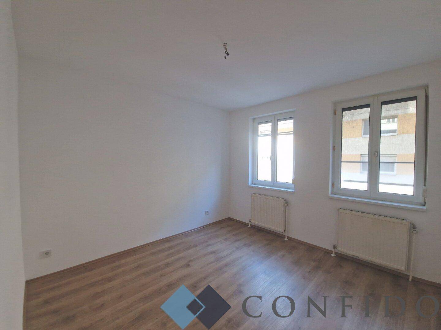 Helles Schlafzimmer mit Laminatboden und zwei Fenstern, bietet eine ruhige und einladende Atmosphäre.