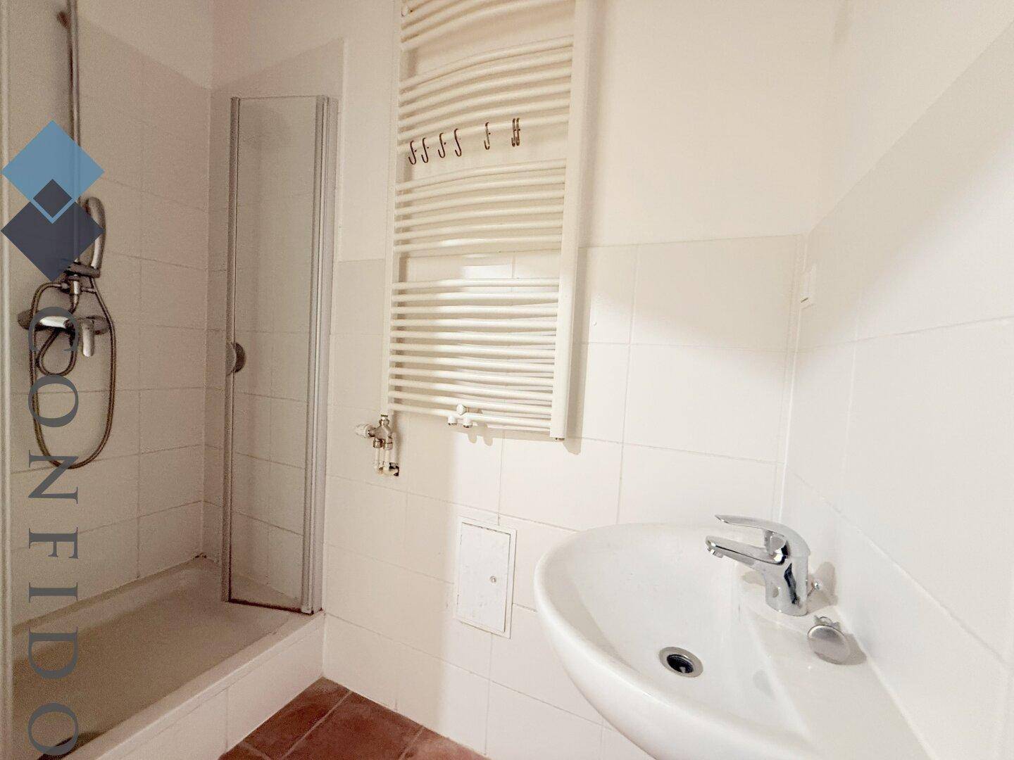 Modernes Badezimmer mit Dusche, Waschbecken und beheiztem Handtuchhalter, hell gefliest.