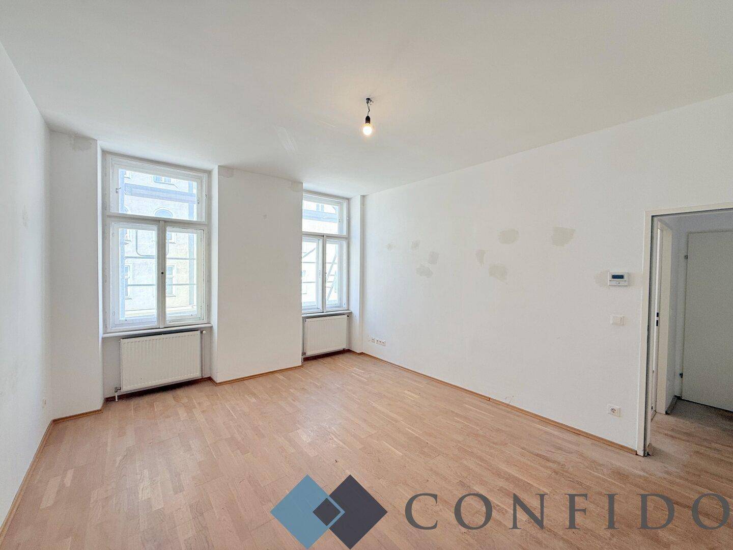 Helles Wohnzimmer mit Parkettboden und zwei großen Fenstern, bereit zur individuellen Gestaltung.