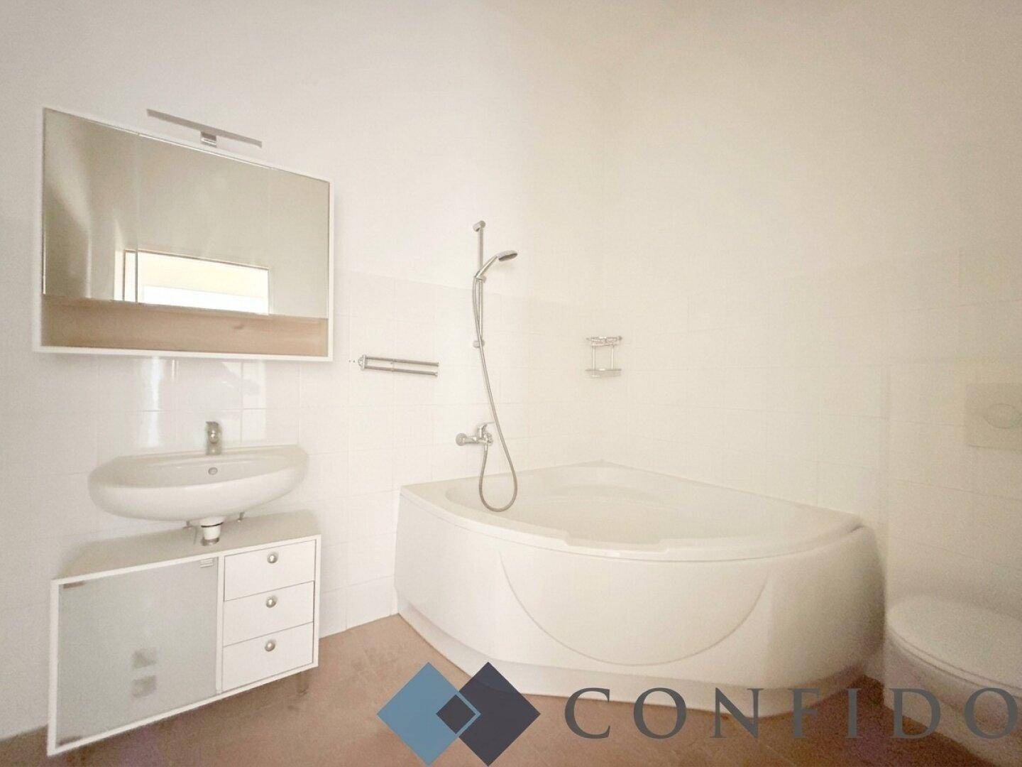 Helles Badezimmer mit Eckbadewanne, Waschbecken mit Unterschrank und Wandspiegel.