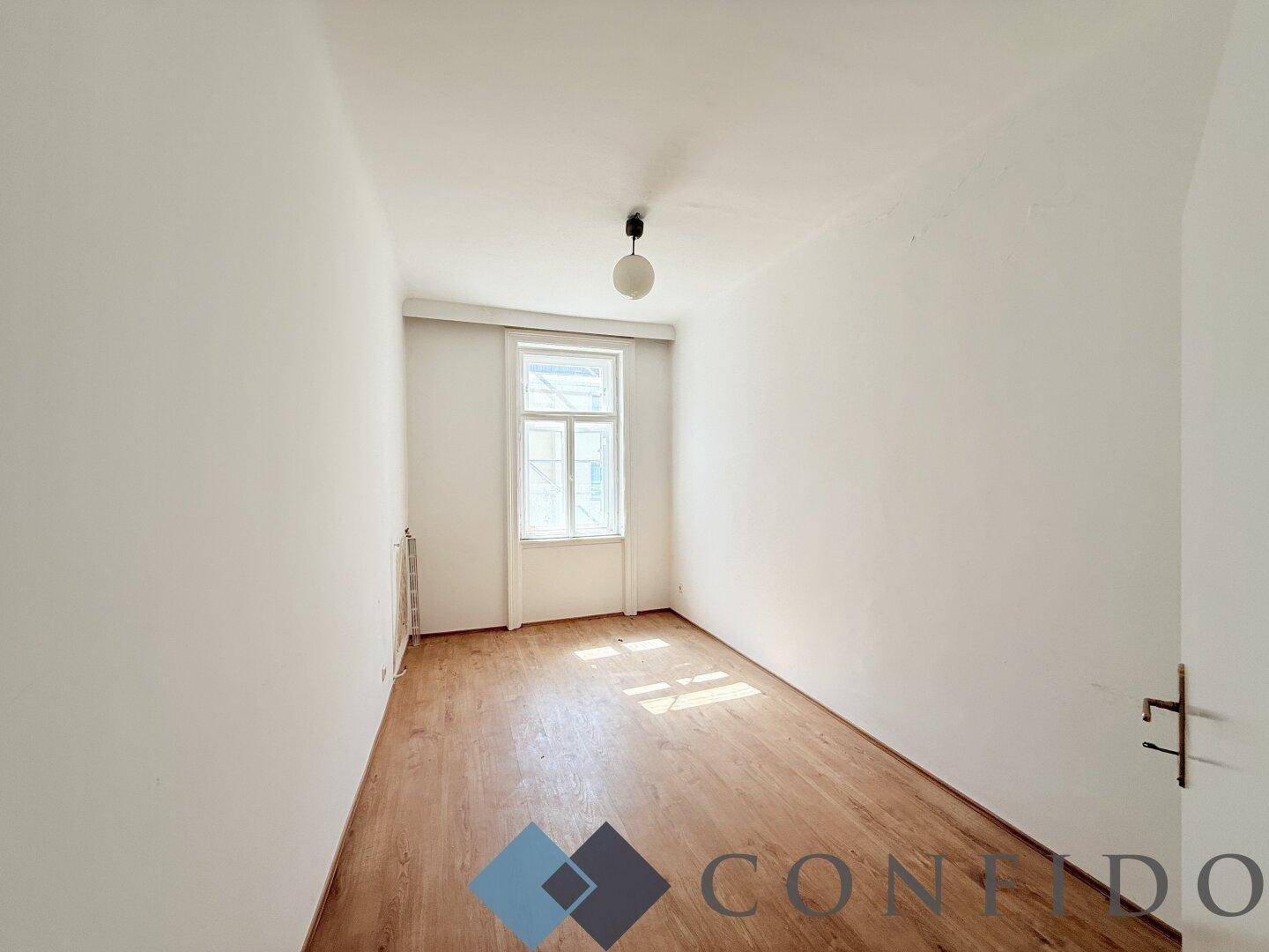 Kleiner, heller Raum mit Holzboden und einem Fenster, ideal als Schlaf- oder Arbeitszimmer.