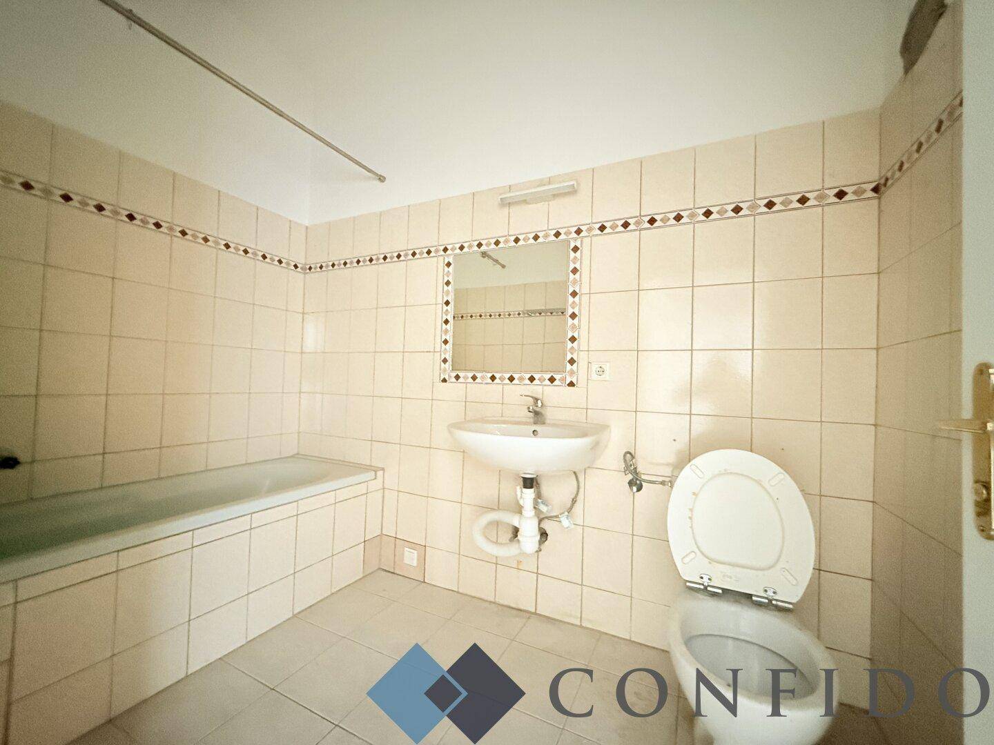 Badezimmer mit beigefarbenen Fliesen, Badewanne, Toilette und Waschbecken in funktionalem Zustand.