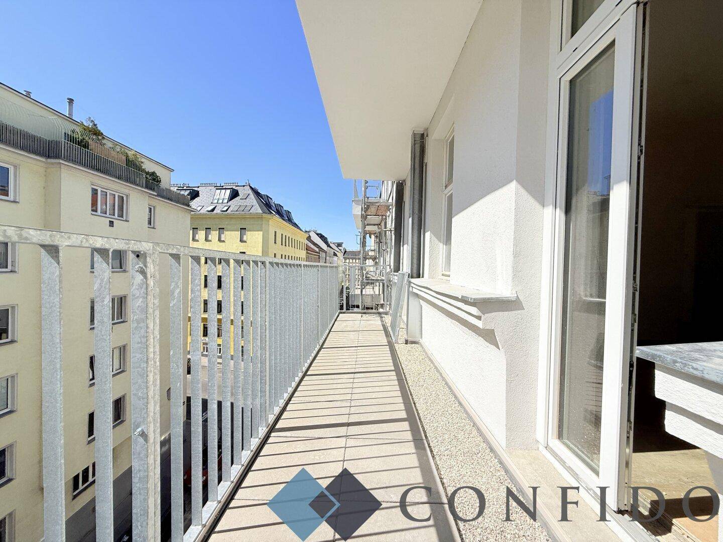 Langer Balkon mit Metallgeländer und Ausblick auf die städtische Umgebung.