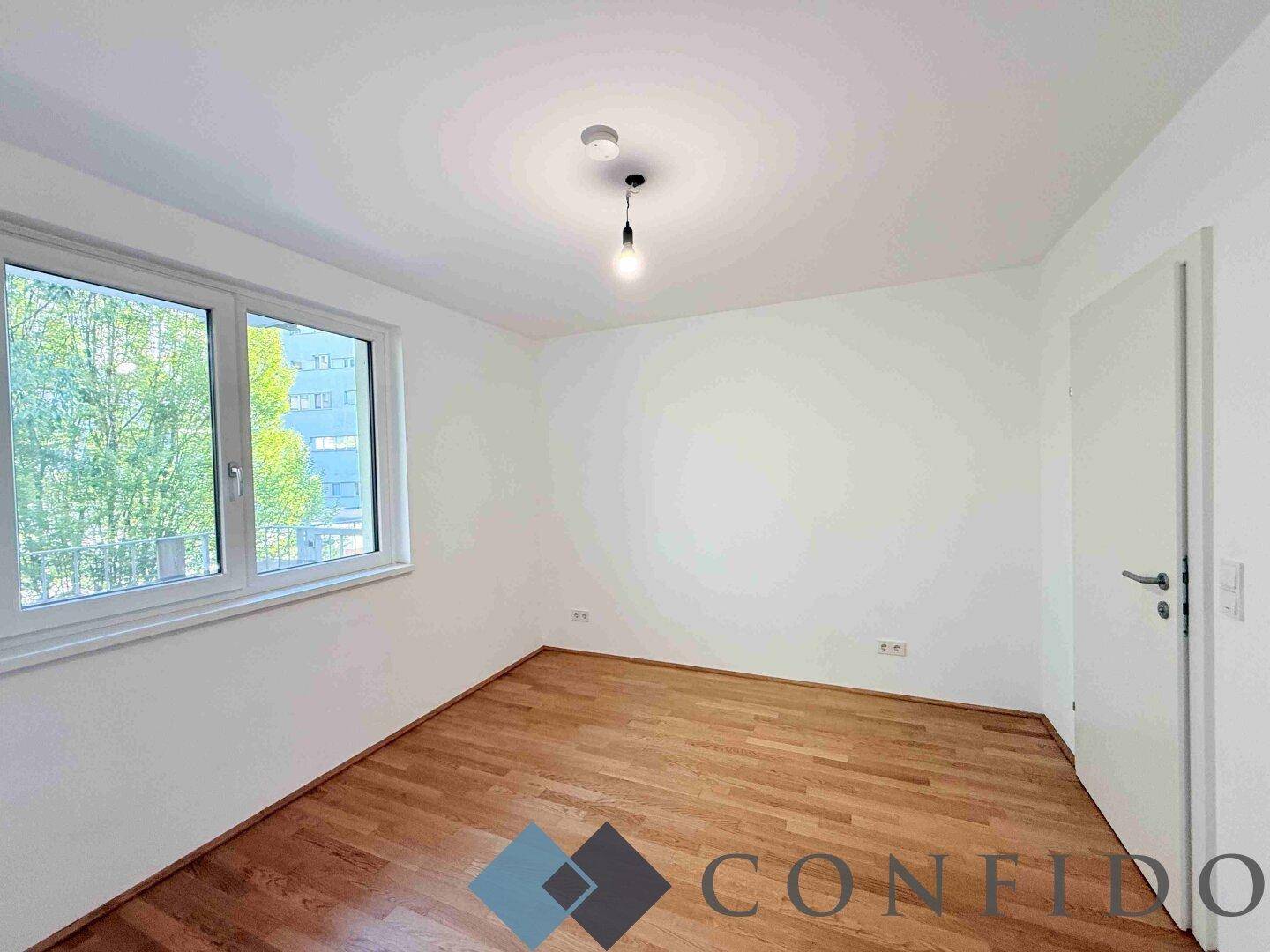 Helles Schlafzimmer mit Parkettboden und Fenster mit Blick ins Grüne.