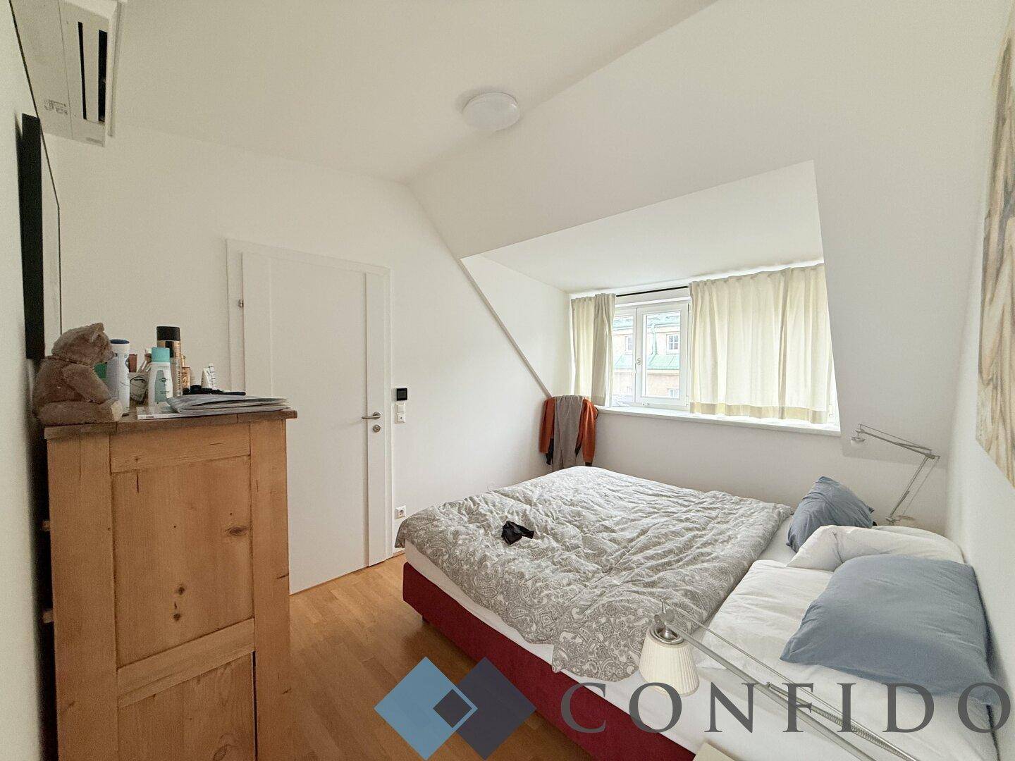 Gemütliches Schlafzimmer mit Holzboden, Dachschräge und Fenster für natürliches Tageslicht.
