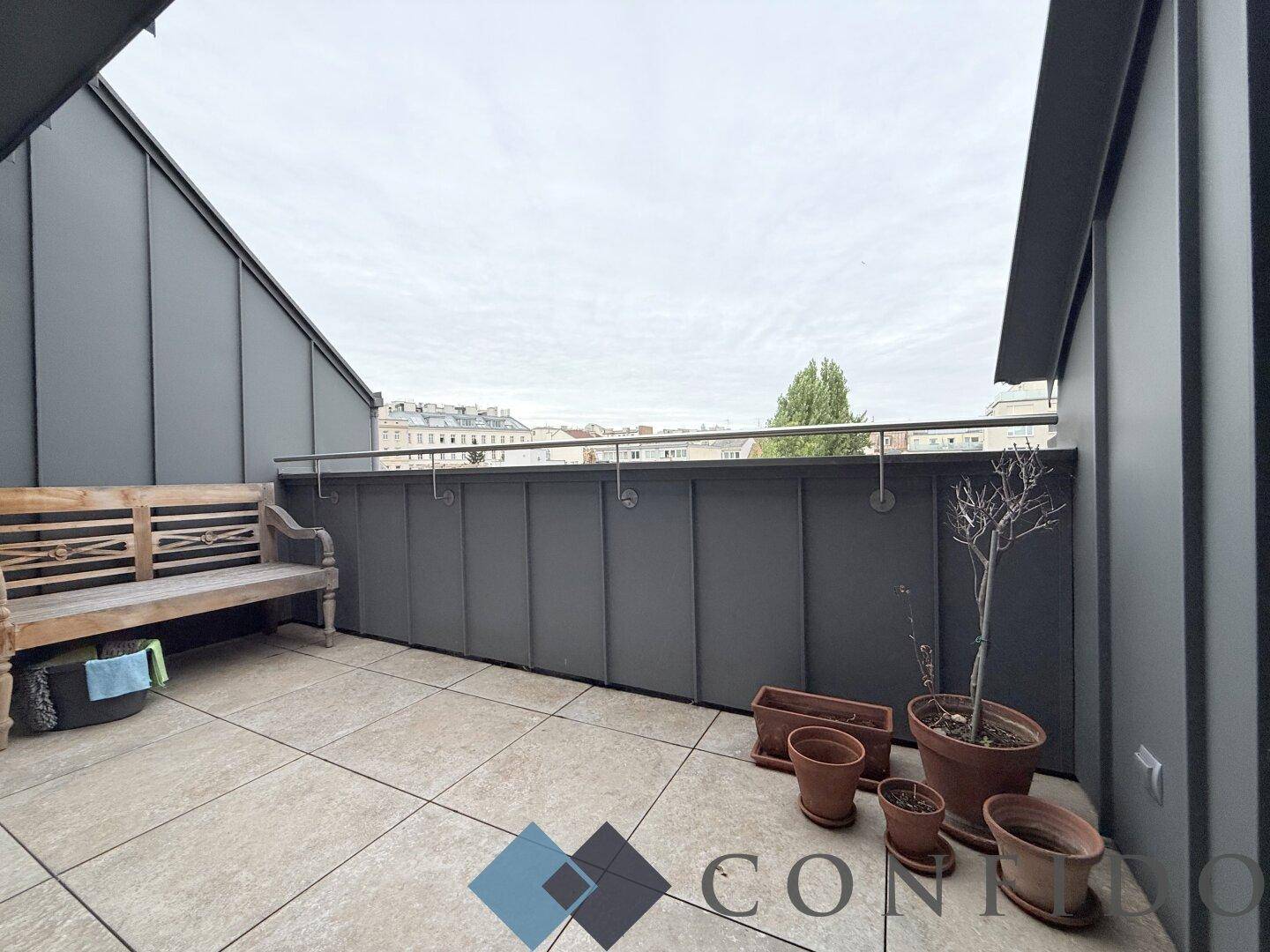 Gemütliche Dachterrasse mit Fliesenboden, Holzsitzbank und weitem Blick über die Stadt.