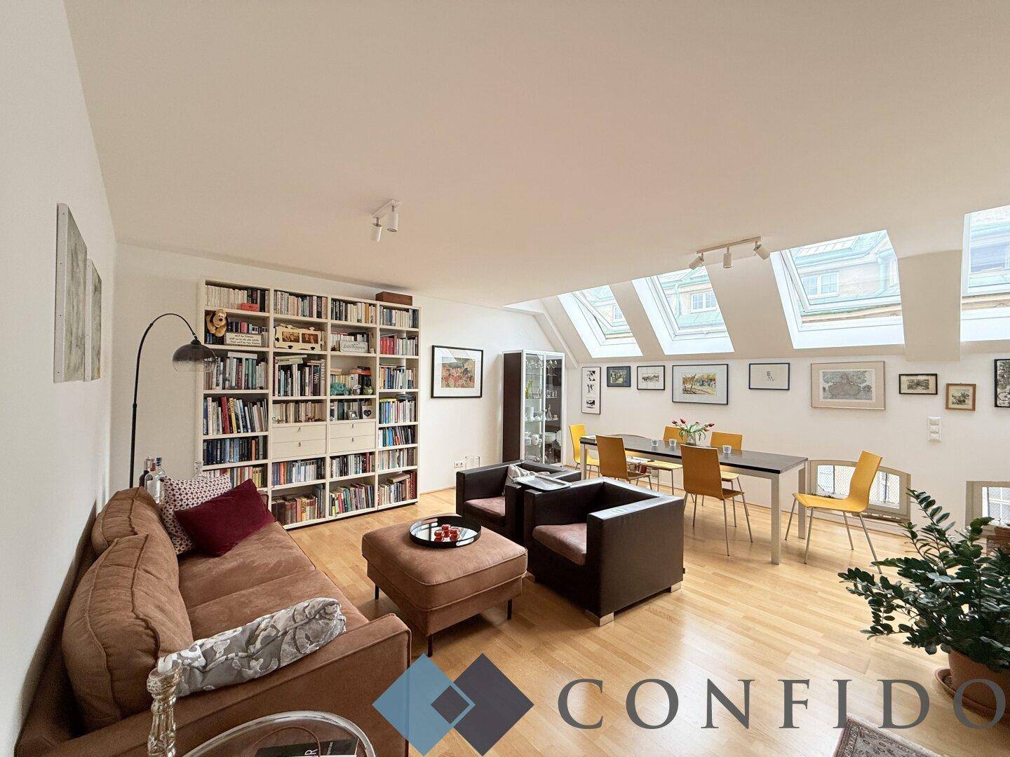 Helles Wohn- und Esszimmer mit Holzboden, großer Bücherwand und mehreren Dachfenstern.