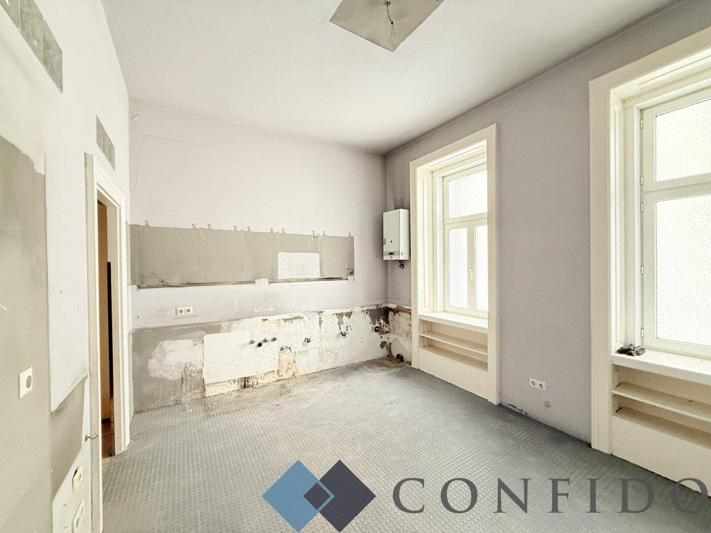 Renovierungsbedürftige Küche mit grauen Wänden, Gastherme und vorbereiteten Anschlüssen für Geräte.