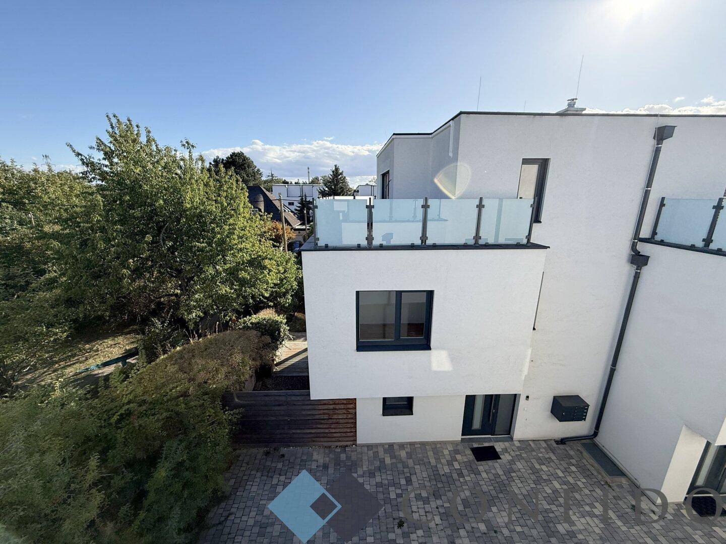 Ansicht des modernen Gebäudes von oben mit gepflastertem Bereich und Balkon mit Glasgeländer.