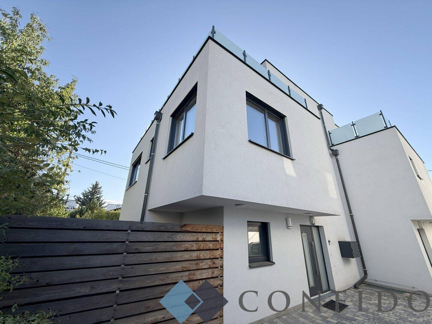 Eingangsbereich des modernen weißen Gebäudes mit dunklen Fenstern und Holzverkleidung.