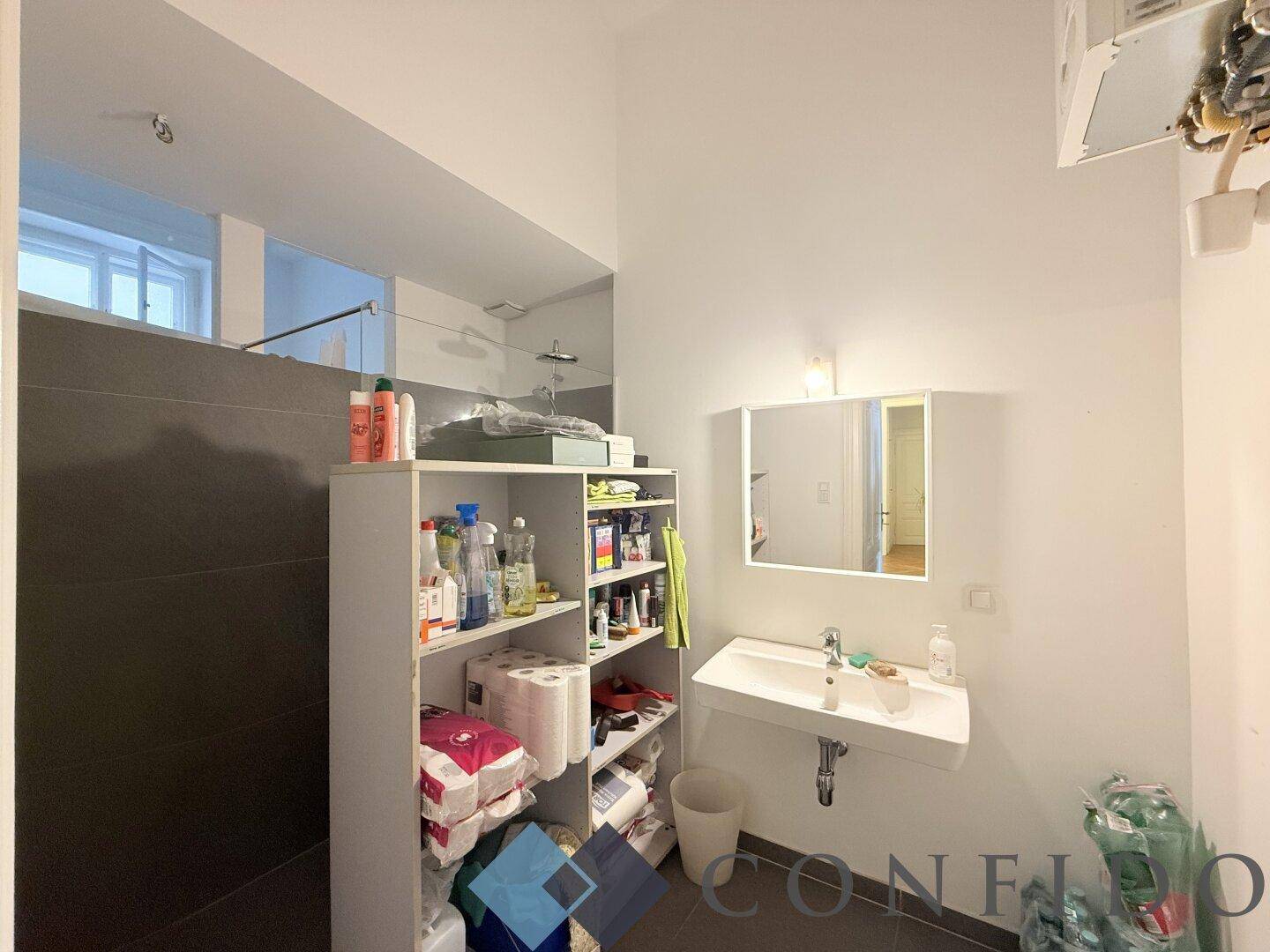 Modernes Badezimmer mit Waschbecken, Spiegelschrank und grauen Fliesen, gut beleuchtet.