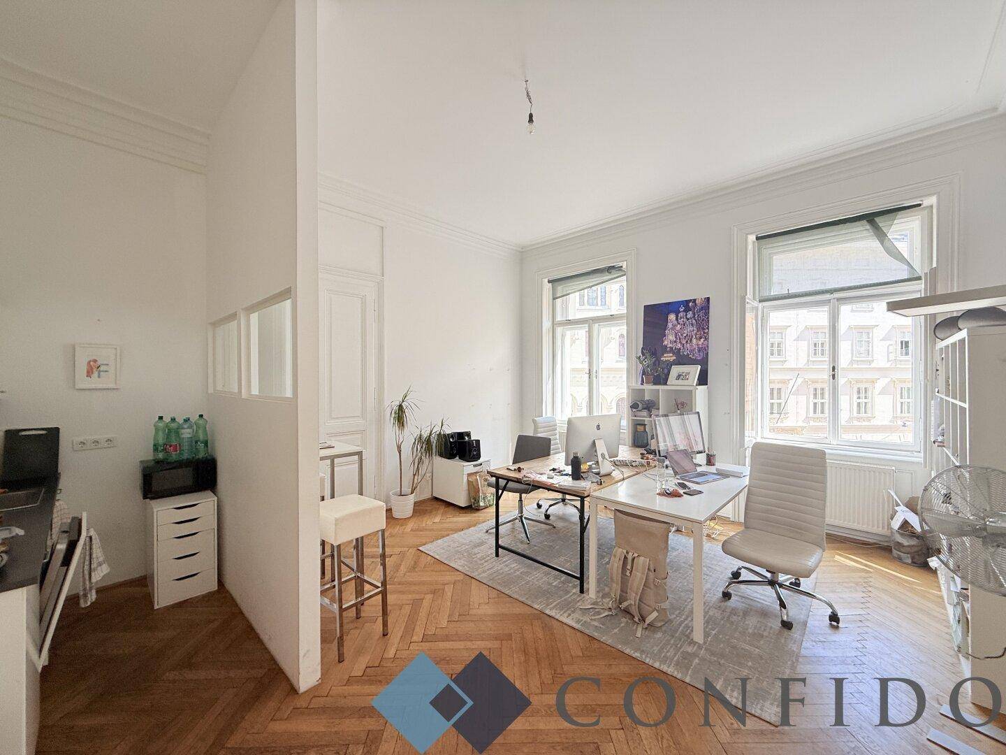 Großes Büro mit zwei Arbeitsplätzen, Fischgrätparkett und Blick auf die Stadt durch die Fenster.