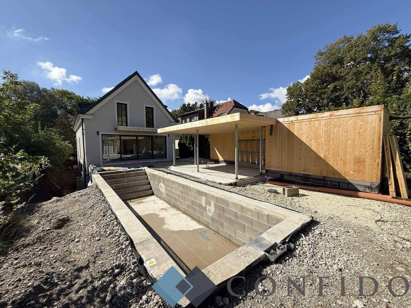Baustelle eines Hauses mit Rohbau des Pools und Holzkonstruktion im Hintergrund.
