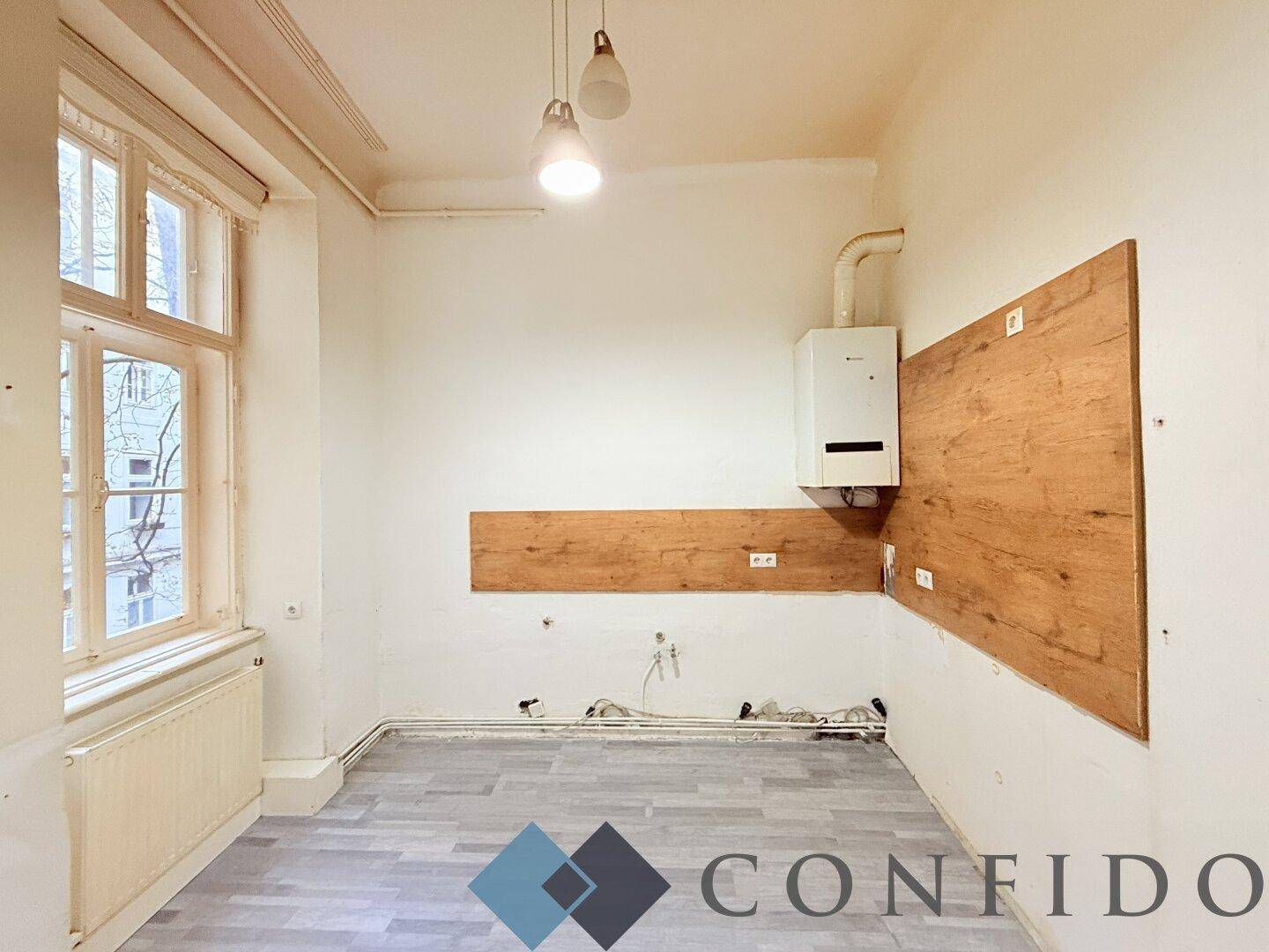 Leere Küche mit Gastherme, Laminatboden und einem Fenster, bereit für die Installation einer Einbauküche.