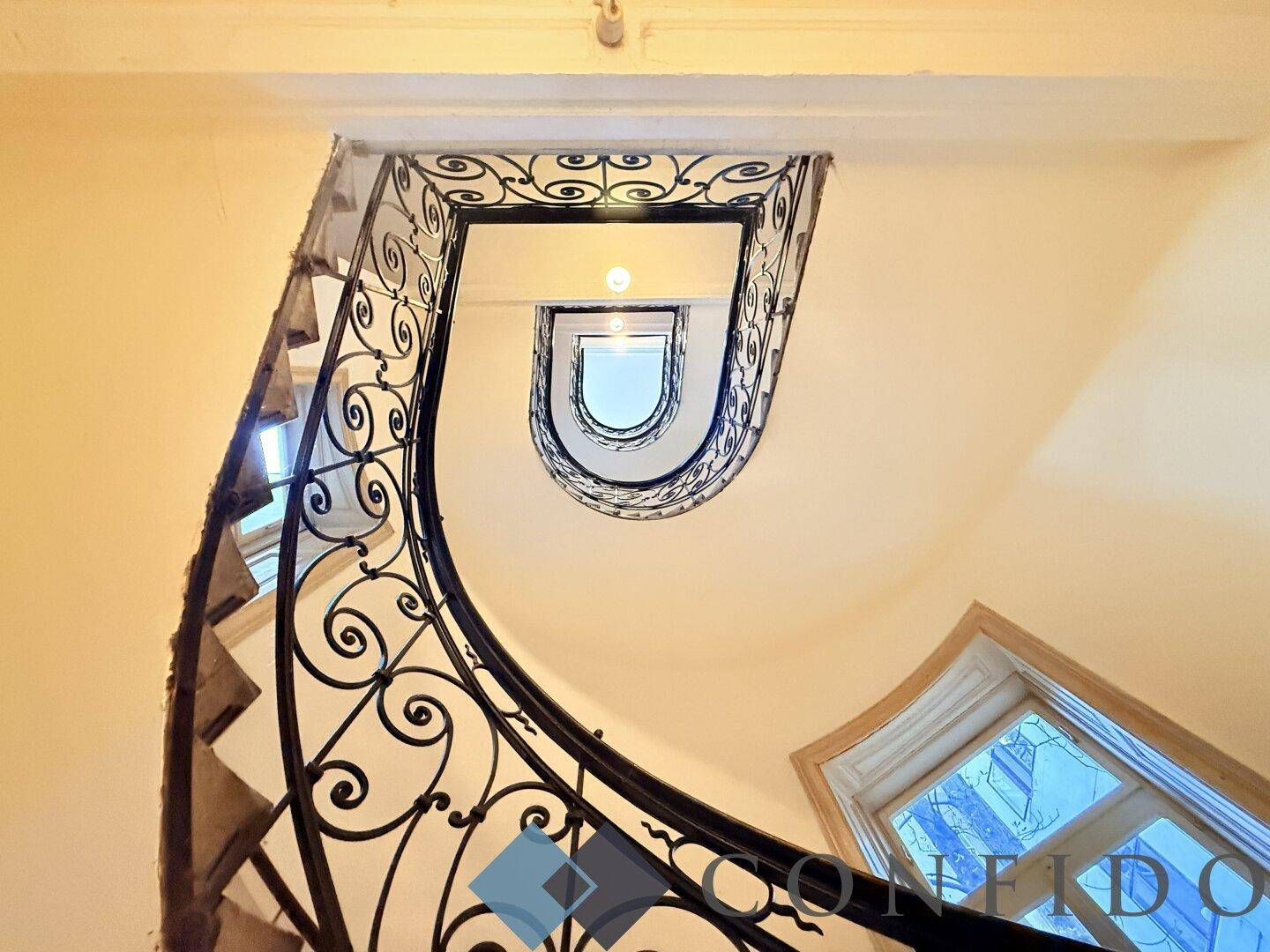 Elegantes Treppenhaus mit schmiedeeisernem Geländer und natürlichem Lichteinfall durch die Fenster.