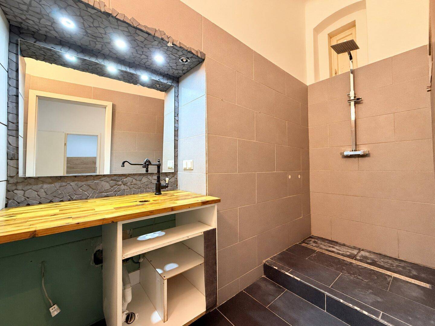 Modernes Badezimmer mit braunen Fliesen, einer begehbaren Dusche und einem Waschtisch mit Holzplatte.