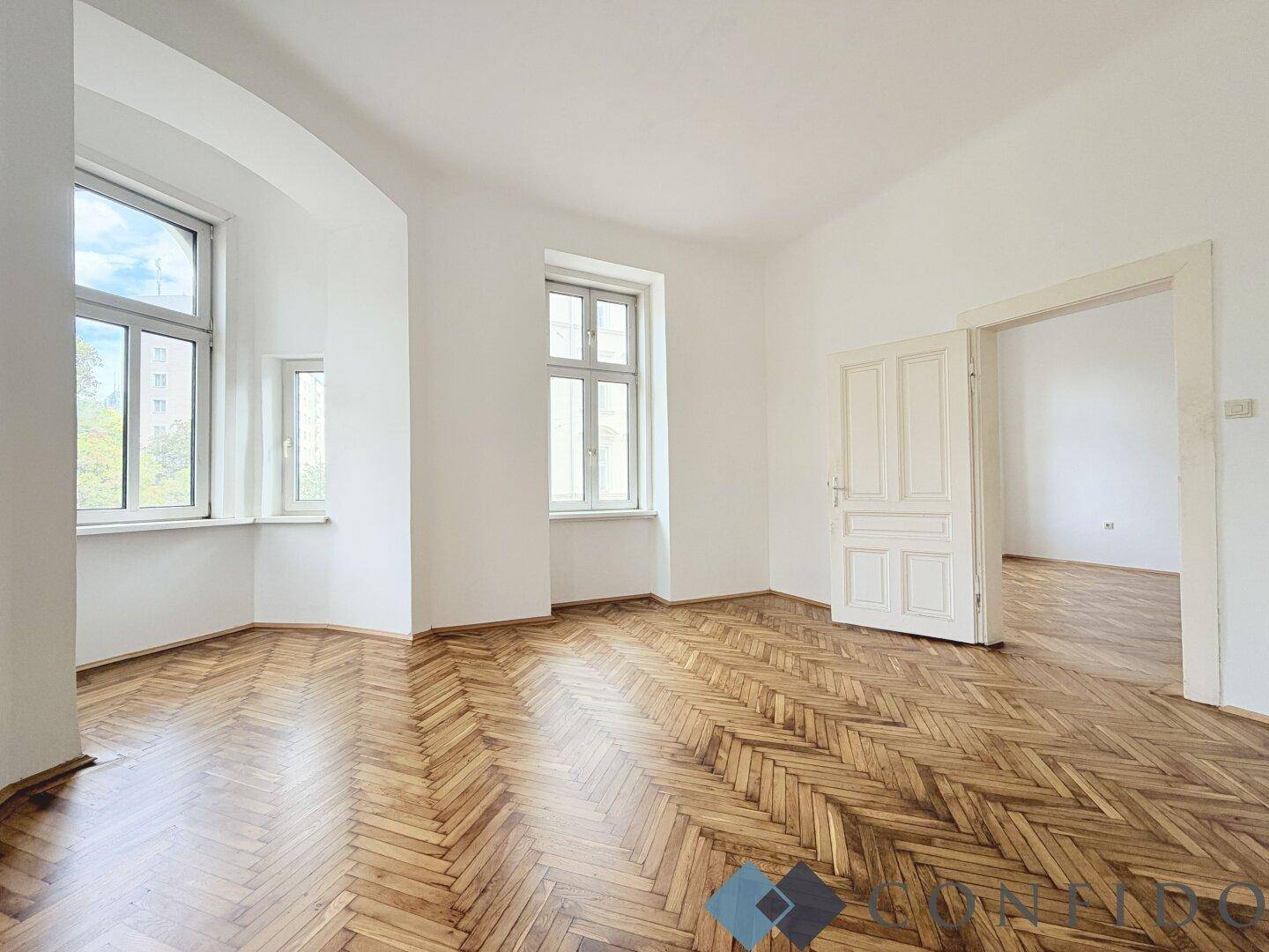 Geräumiges Zimmer mit klassischem Fischgrätparkett und doppelter Flügeltür zu einem weiteren Raum.
