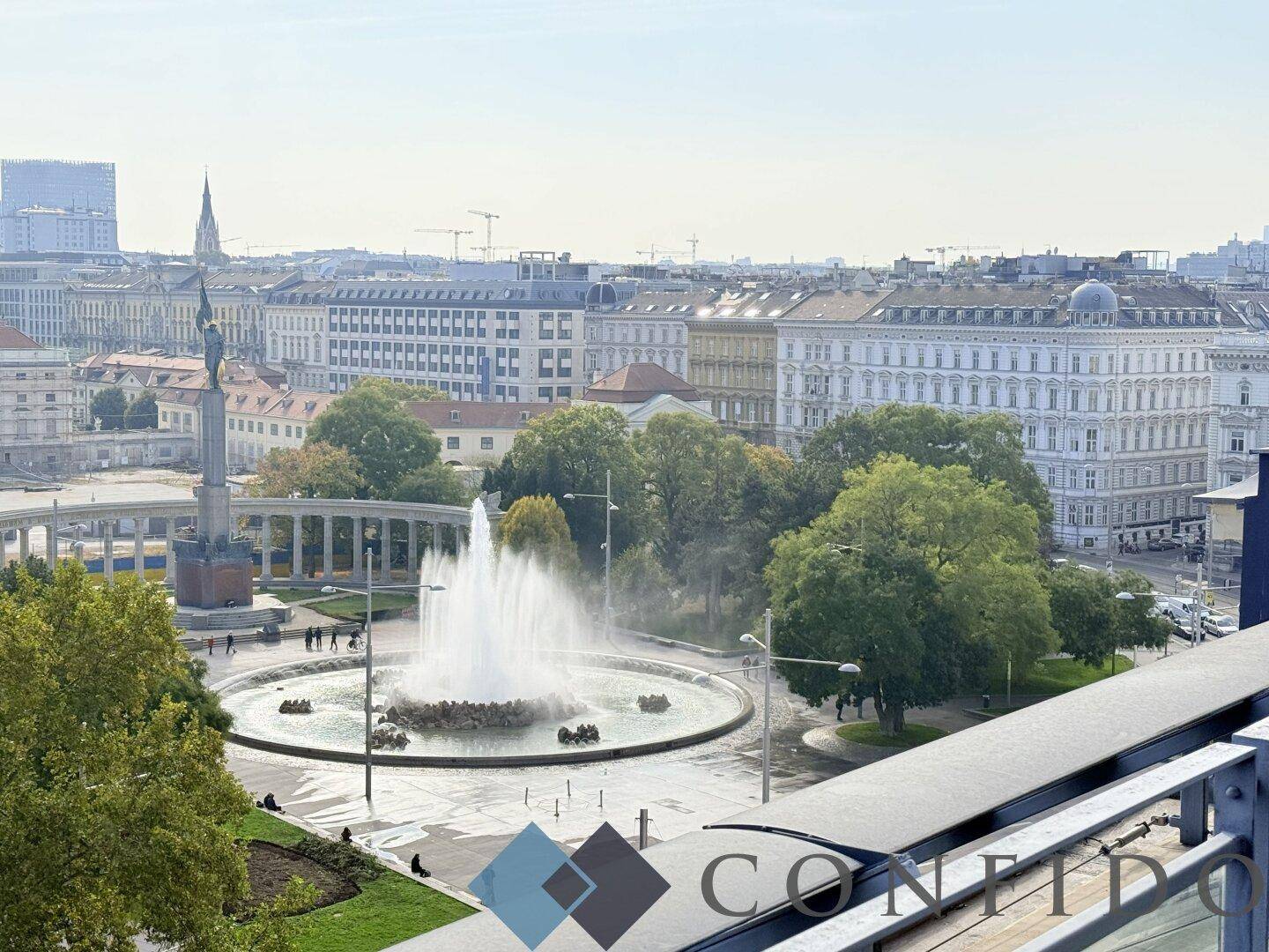 Panoramablick auf die Stadt mit Springbrunnen und historischen Gebäuden unter blauem Himmel.