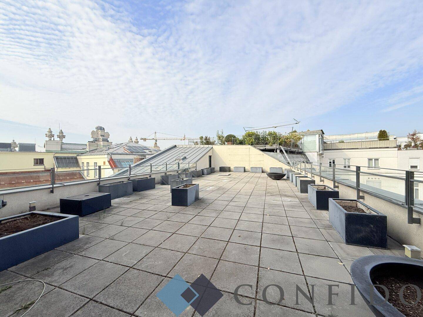Weitläufige Dachterrasse mit Fliesenboden und Pflanzkübeln unter einem bewölkten Himmel.