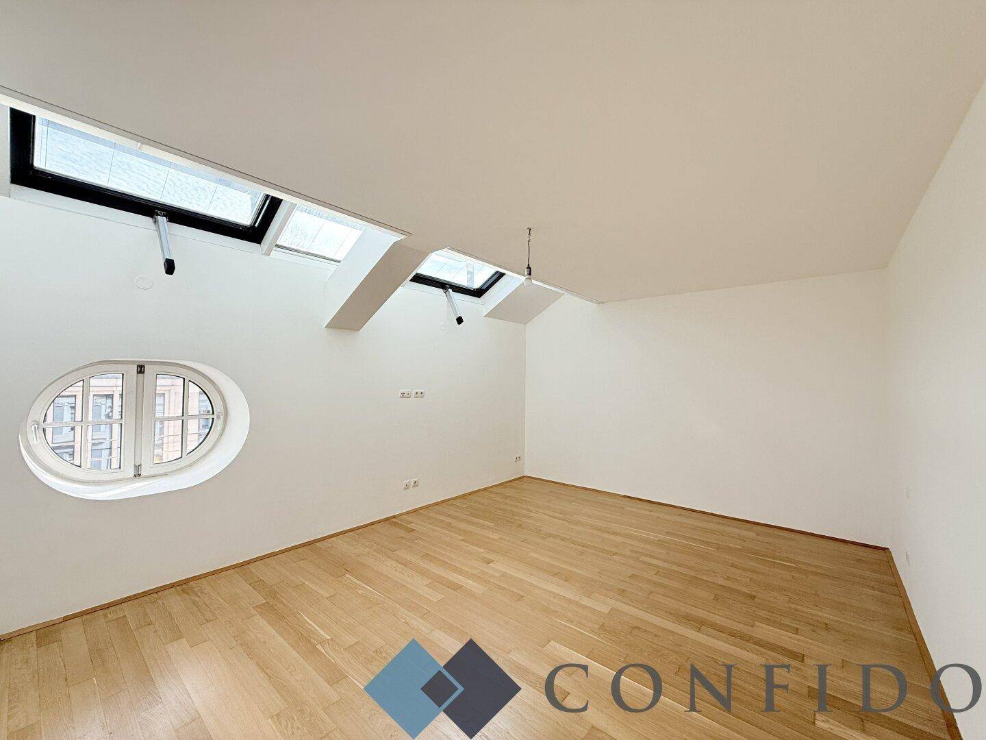 Lichtdurchflutetes Dachzimmer mit Holzboden, mehreren Dachfenstern und runden Fenstern.