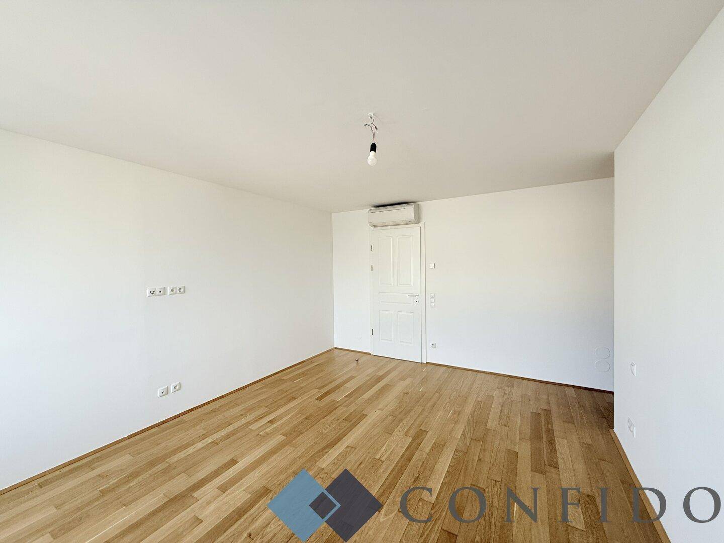 Geräumiges, leeres Zimmer mit Holzboden und Klimaanlage, ideal als Schlafzimmer.