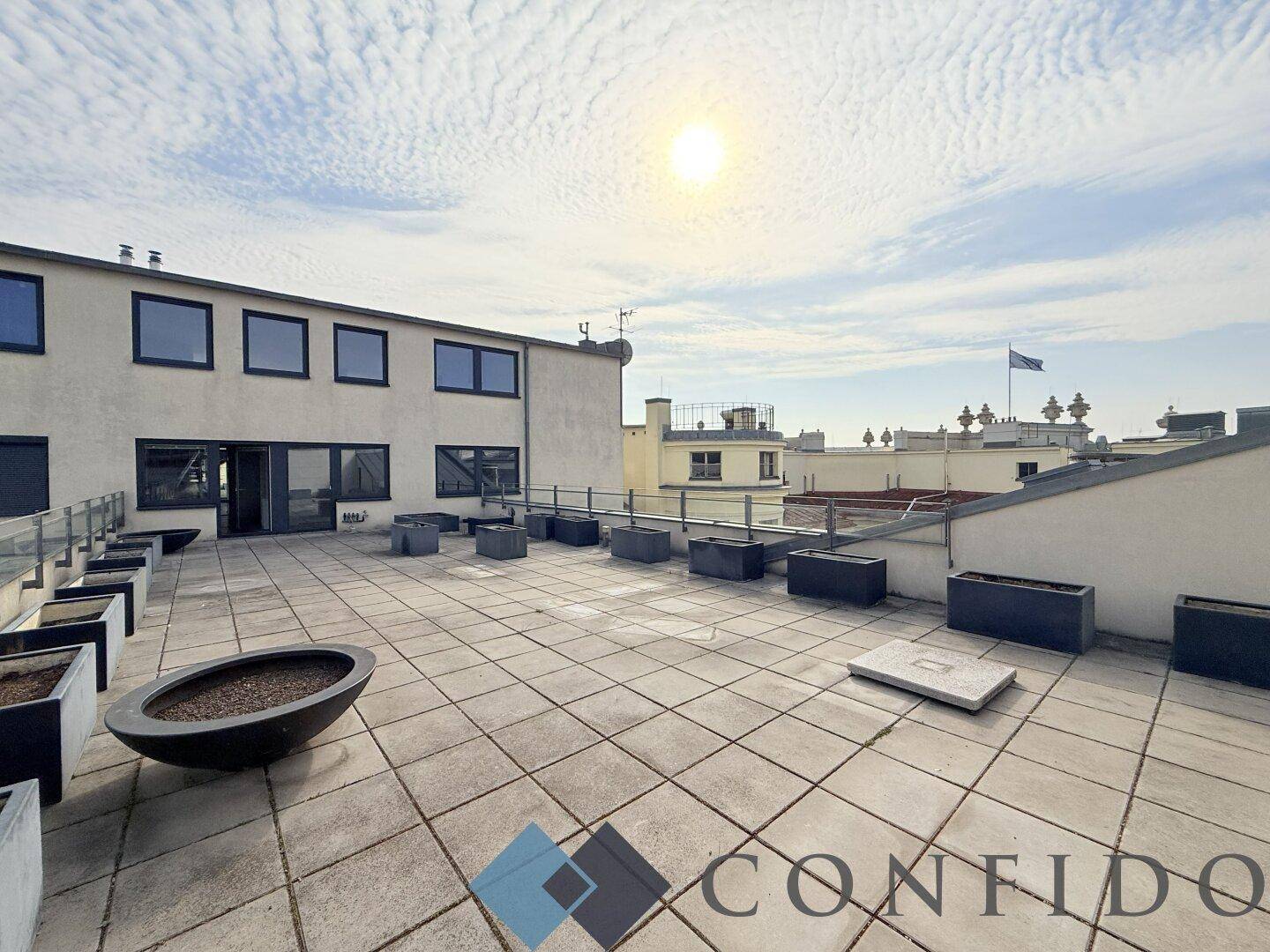 Weitläufige Dachterrasse mit Fliesenboden und Pflanzkübeln unter einem bewölkten Himmel.