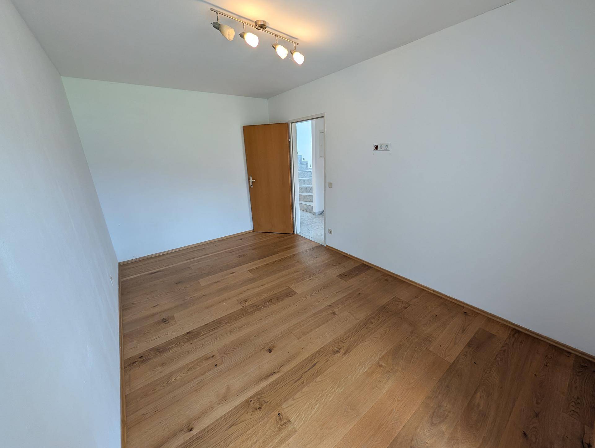 Helles Zimmer mit Holzboden und weiß gestrichenen Wänden, bereit zur individuellen Gestaltung.