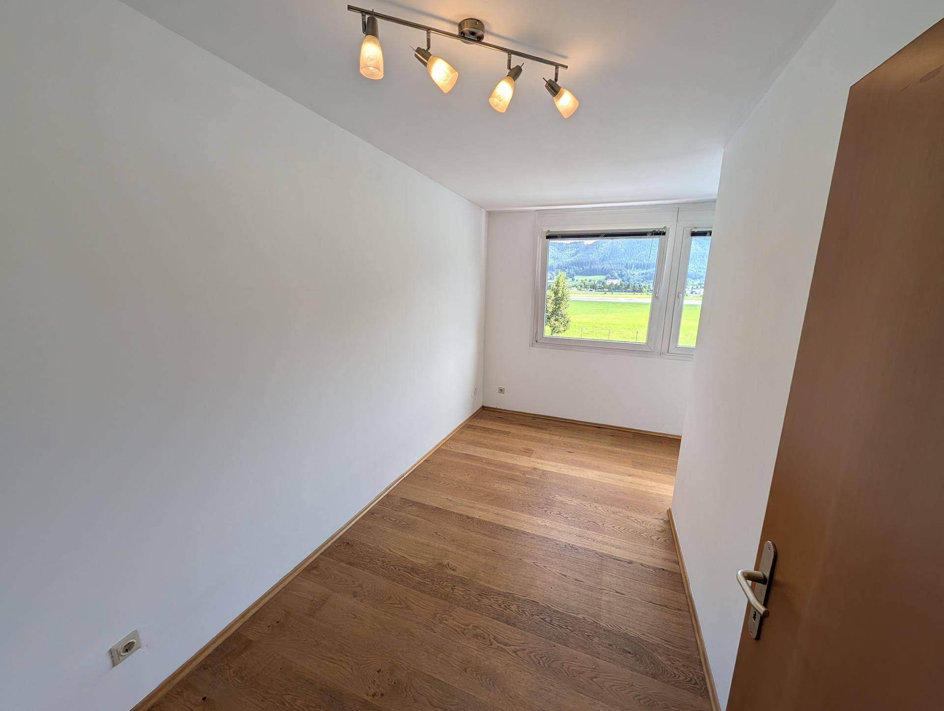 Geräumiges Schlafzimmer mit Holzboden und Fenster, das einen weiten Blick ins Grüne bietet.