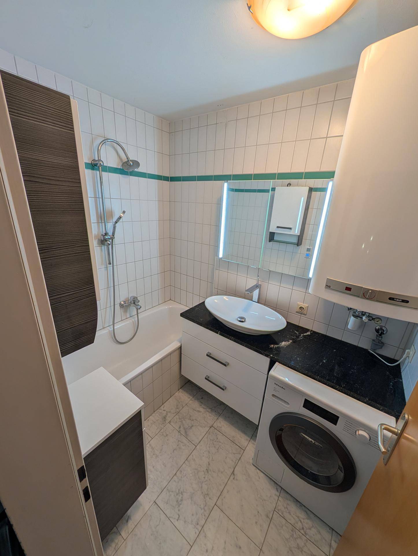 Modernes Badezimmer mit Badewanne, Waschbecken, Waschmaschine und dunkler Granit-Arbeitsplatte.