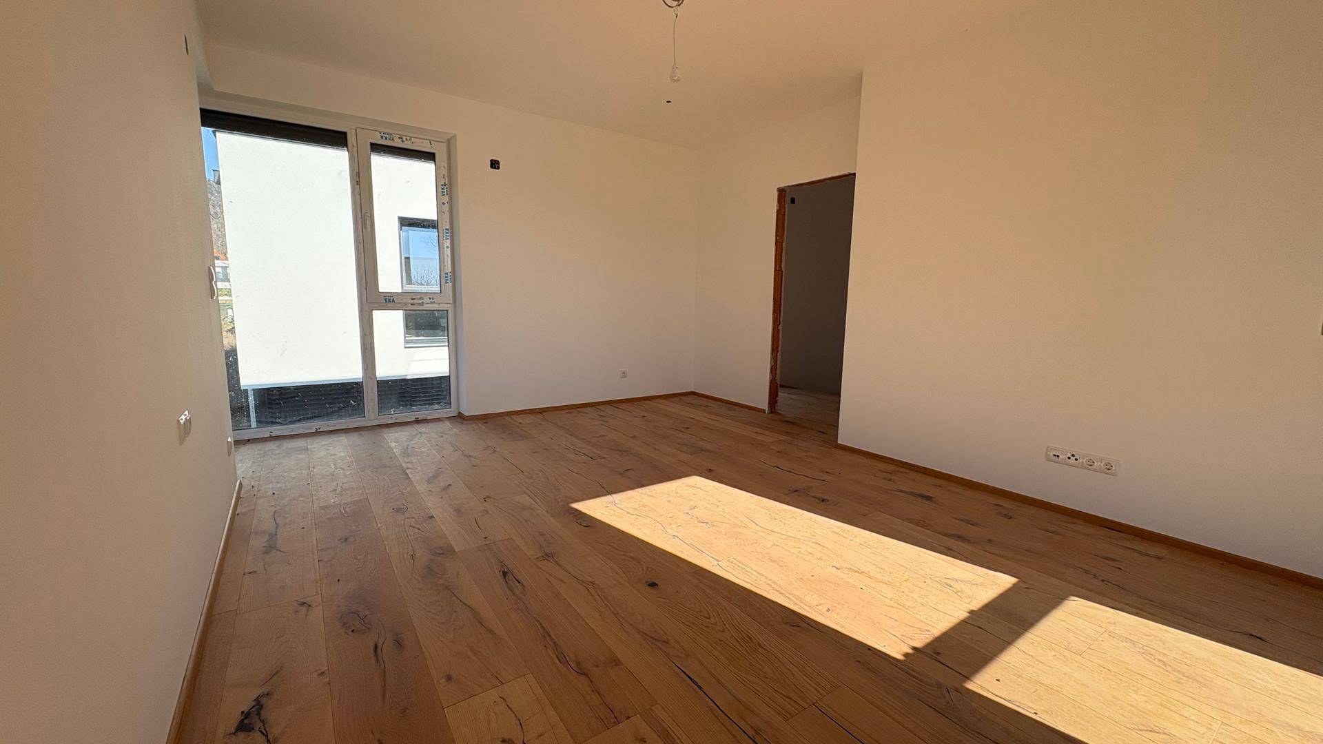 Geräumiges, unmöbliertes Zimmer mit Holzboden und großem Fenster, ideal für individuelle Gestaltung.